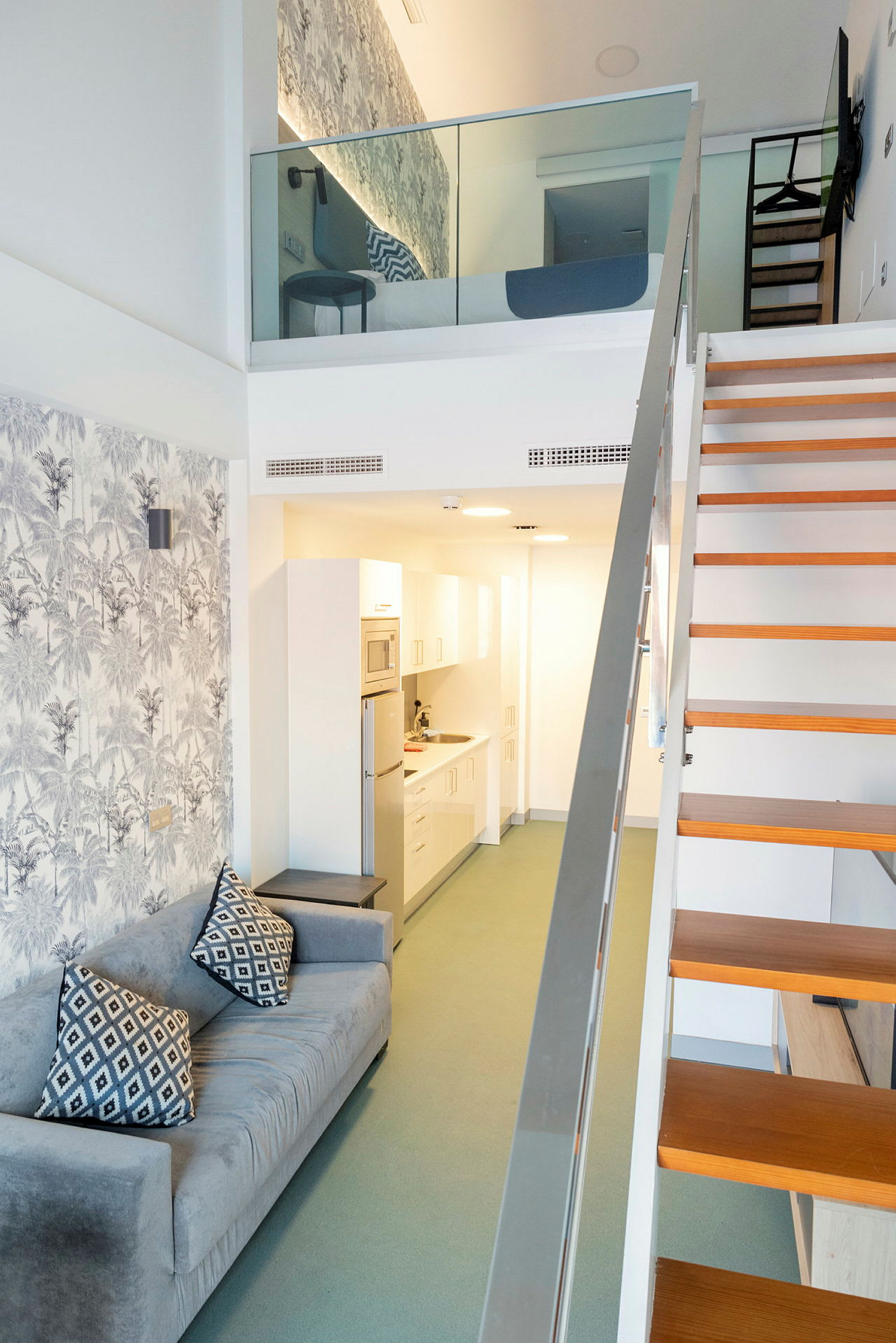 Tvåvåningsrum med en soffa och köksdel på bottenvåningen samt sovdel på övervåningen. (AI-genererad text)