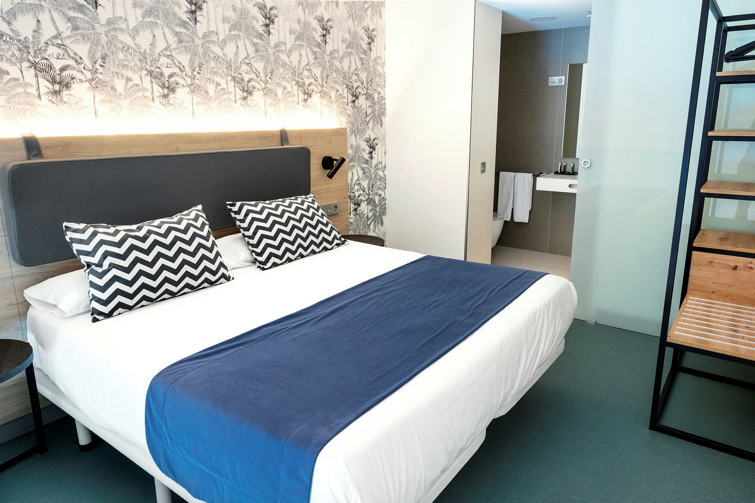 En modern hotellrum med dubbelsäng, blå överkast och två mönstrade kuddar. (AI-genererad text)