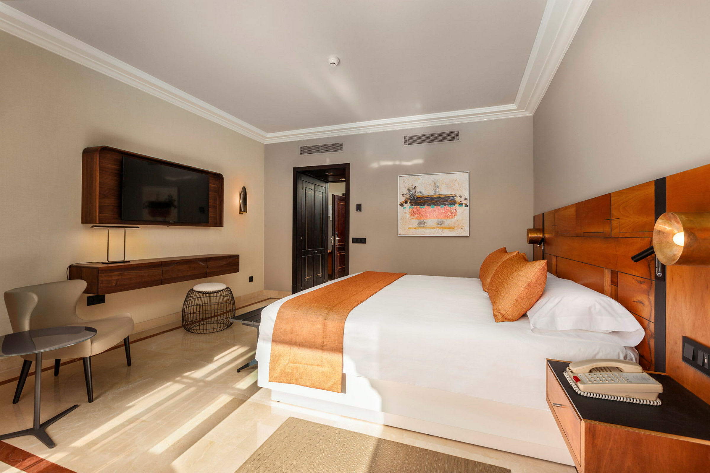 Hotellrum med en stor säng, orange sängkläder och en modern inredning. En TV är monterad på väggen. (AI-genererad text)