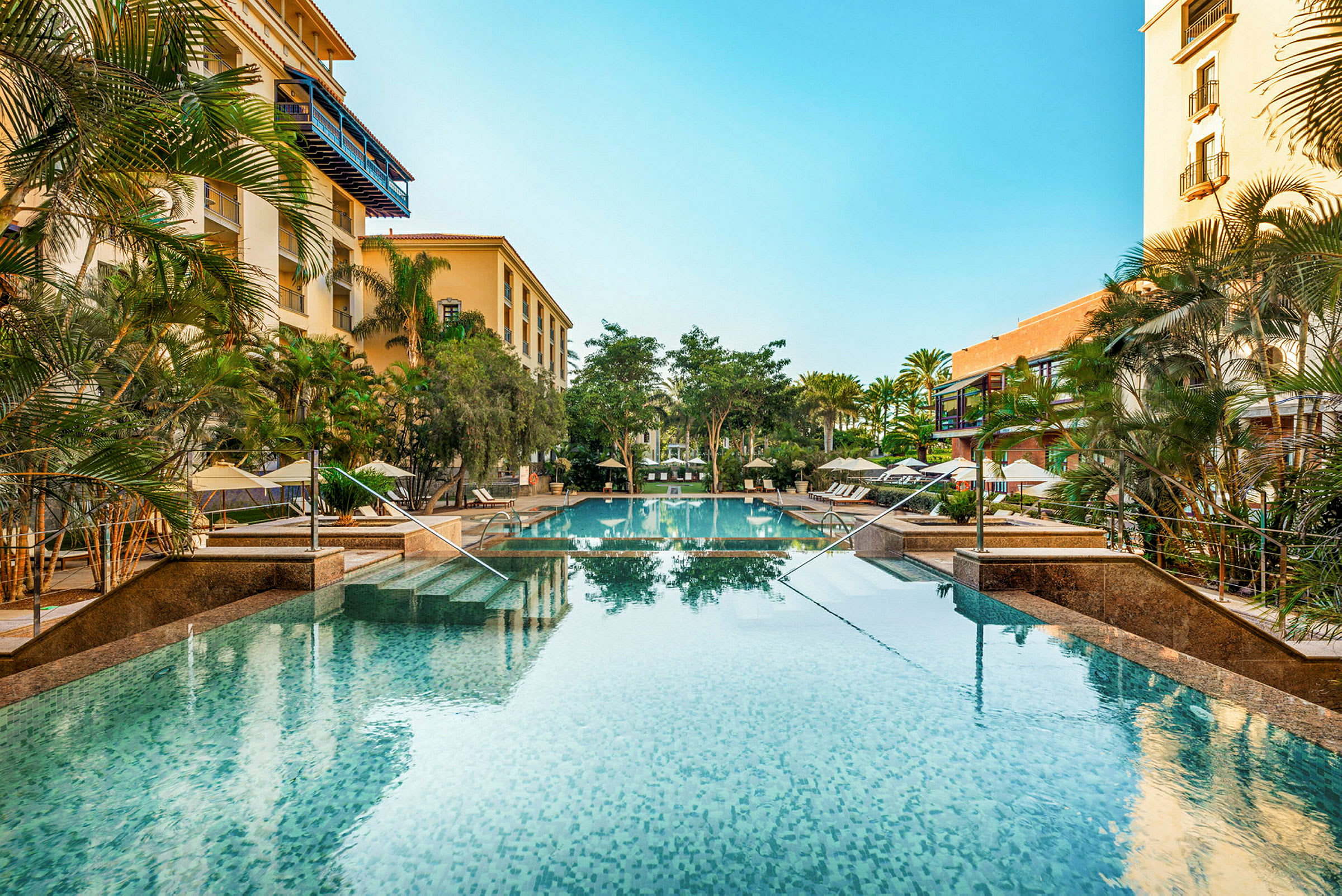 Hotellpool med omgivande grönska och byggnader. (AI-genererad text)