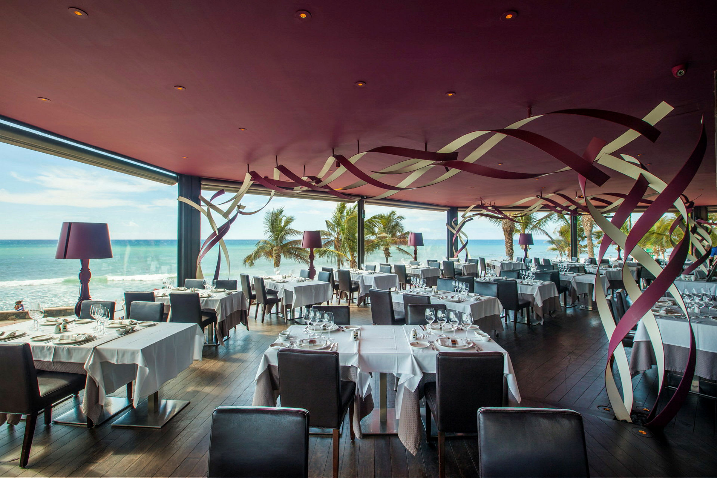 En restaurang med havsutsikt, fylld med väldukade bord och modern inredning. (AI-genererad text)