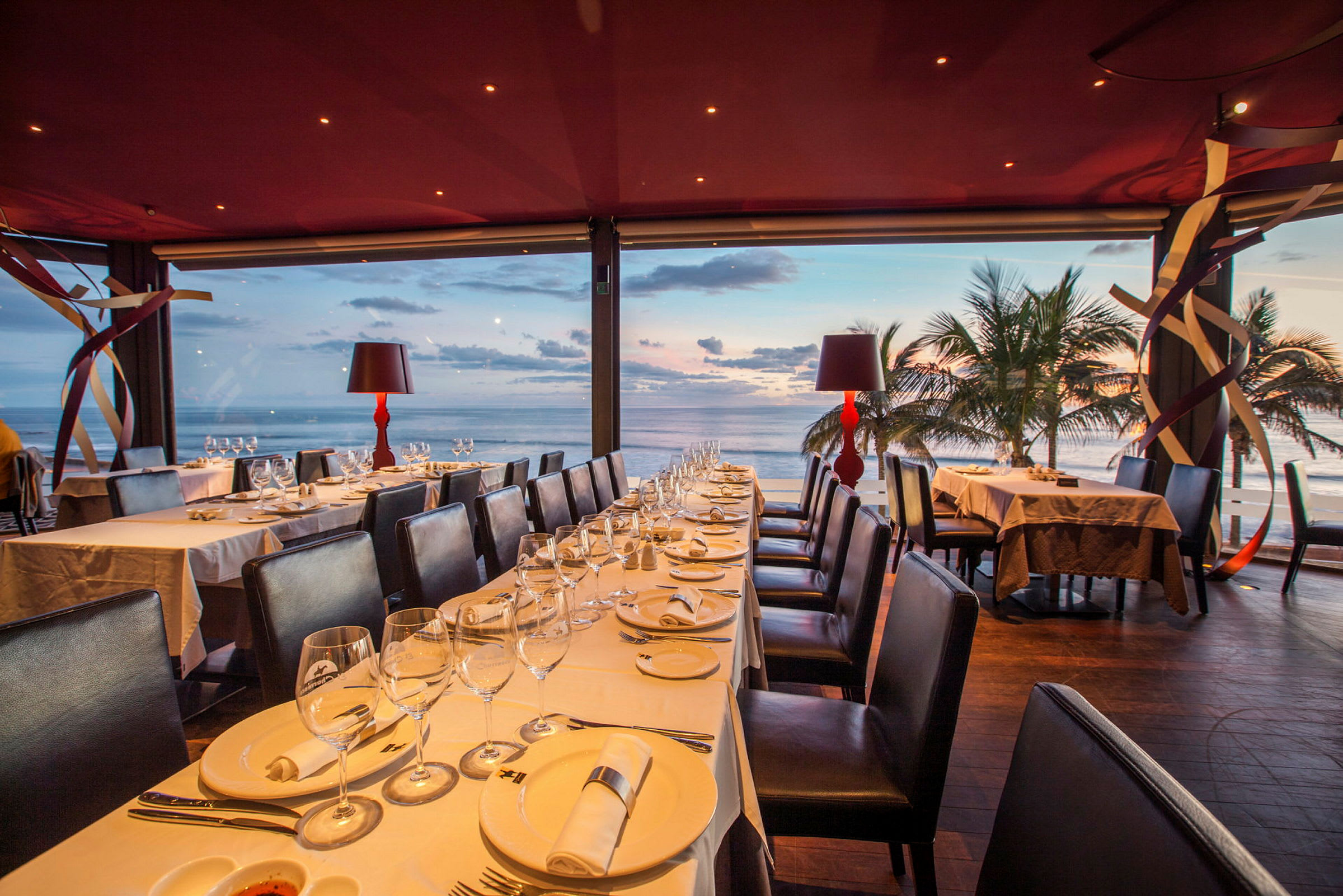 En restaurang med dukade bord och utsikt över havet vid solnedgången. (AI-genererad text)