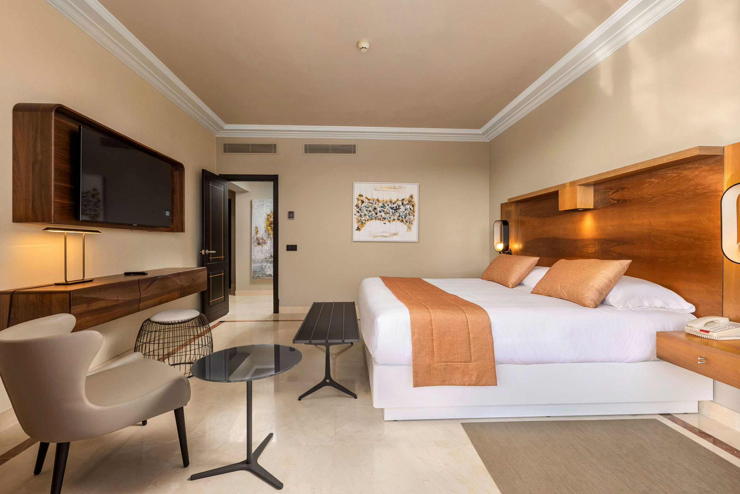 Ett hotellrum med en stor dubbelsäng, en vägghängd TV, en fåtölj och ett sidobord. (AI-genererad text)