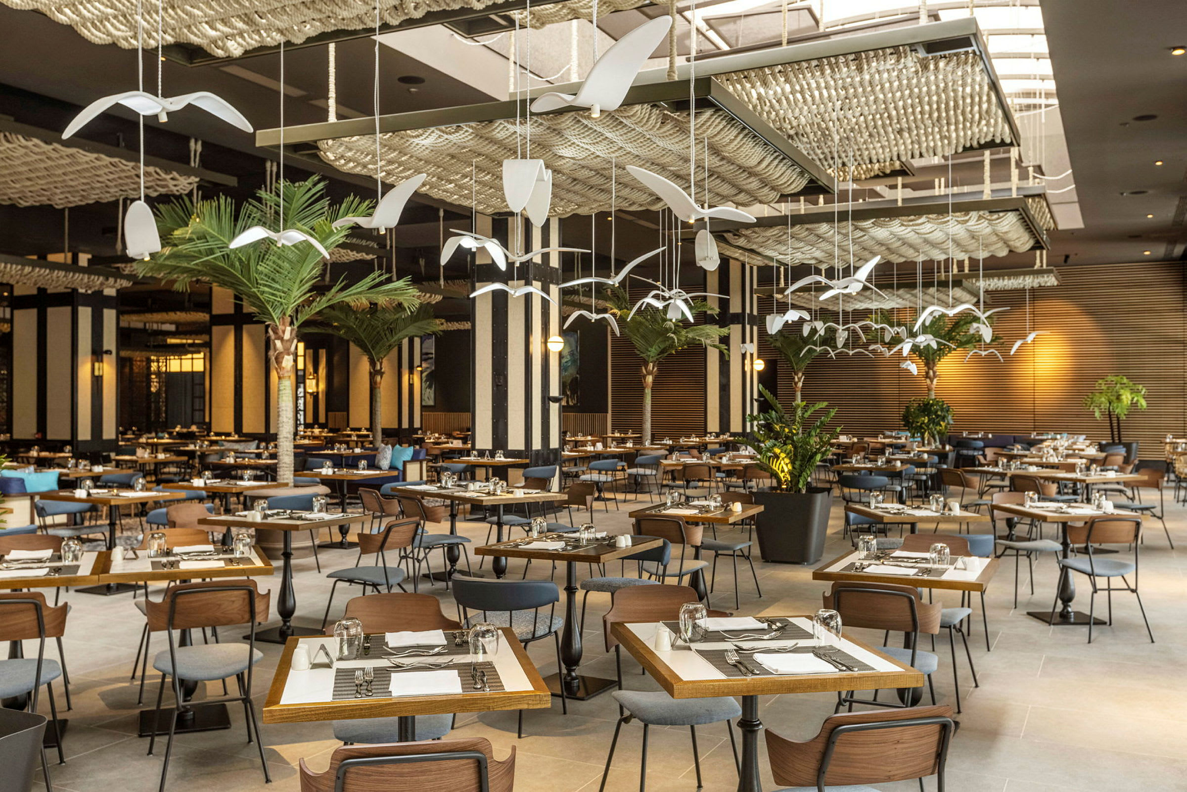Restaurang med många bord och stolar, dekorerad med konstnärliga hängande element och grönska. (AI-genererad text)