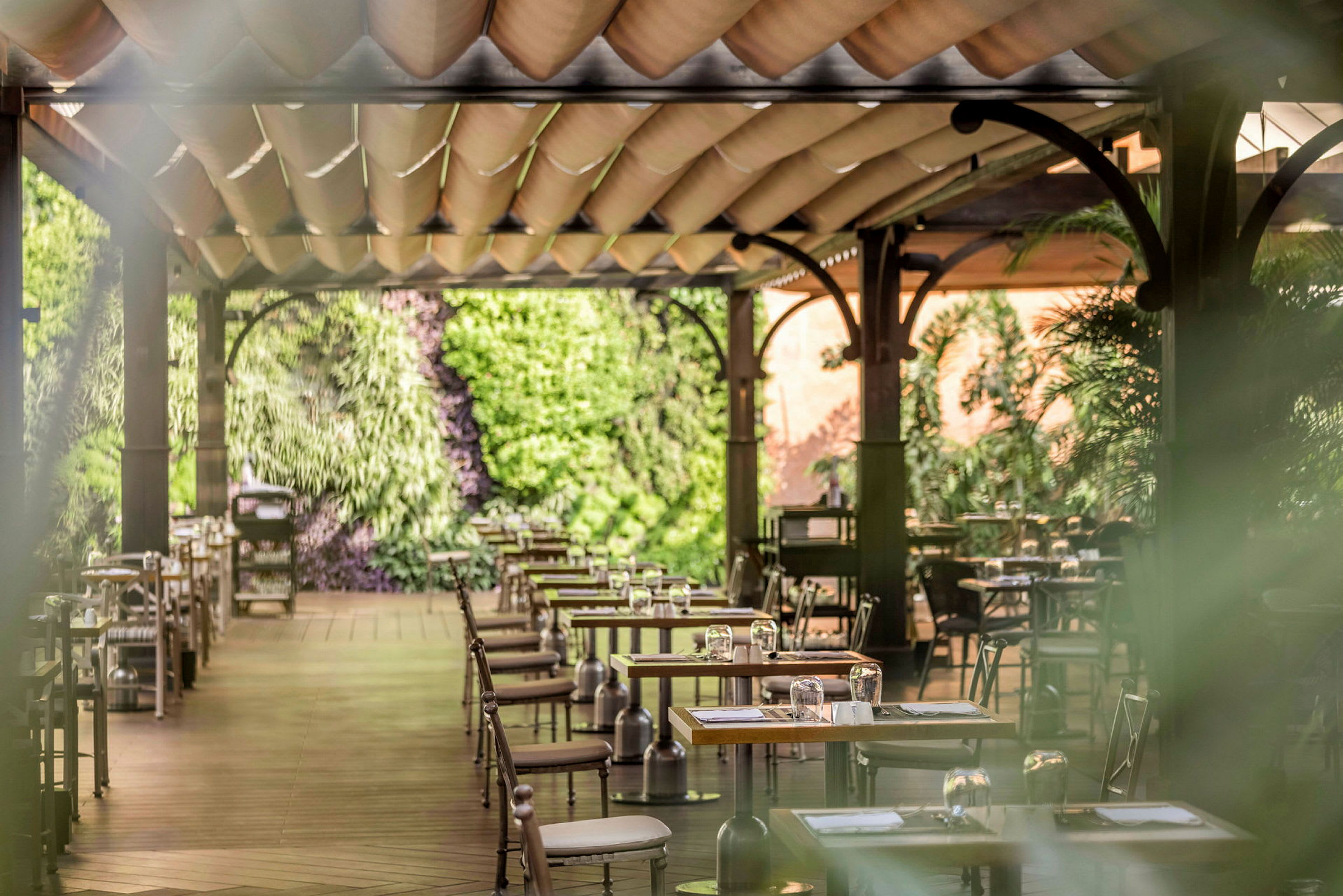 En terrassrestaurang med träbord och stolar, dekorerad med gröna växter. (AI-genererad text)
