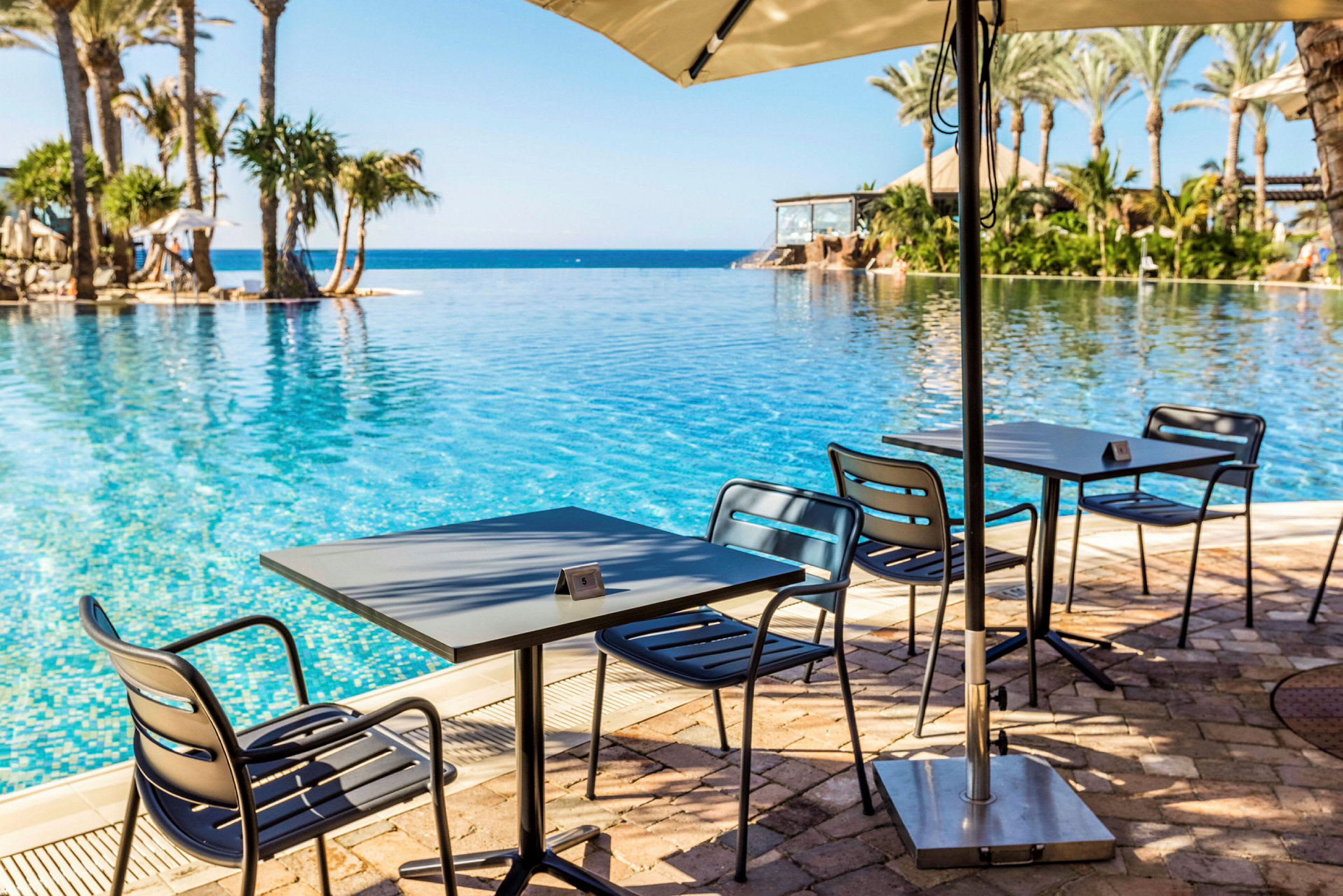 Ett område vid en pool med bord och stolar samt utsikt över havet. (AI-genererad text)