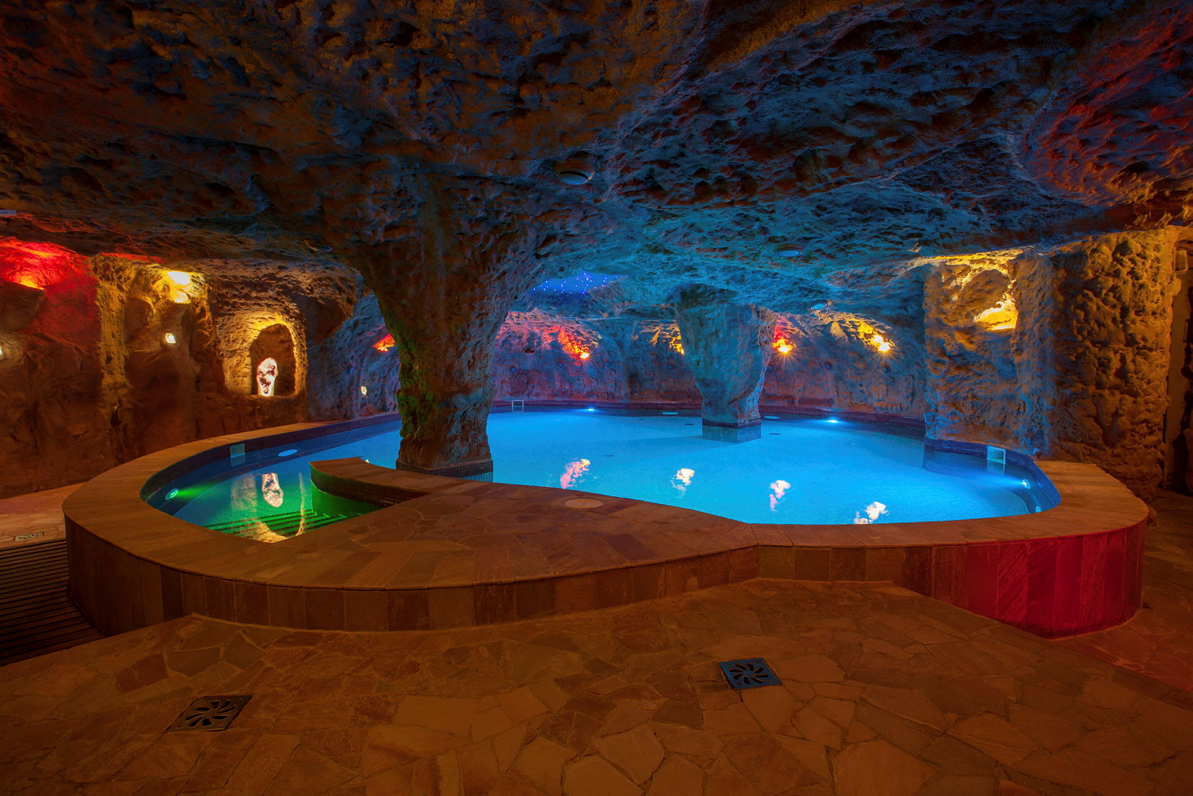 Ett underjordiskt spa med en pool och belysning som skapar en grottliknande atmosfär. (AI-genererad text)