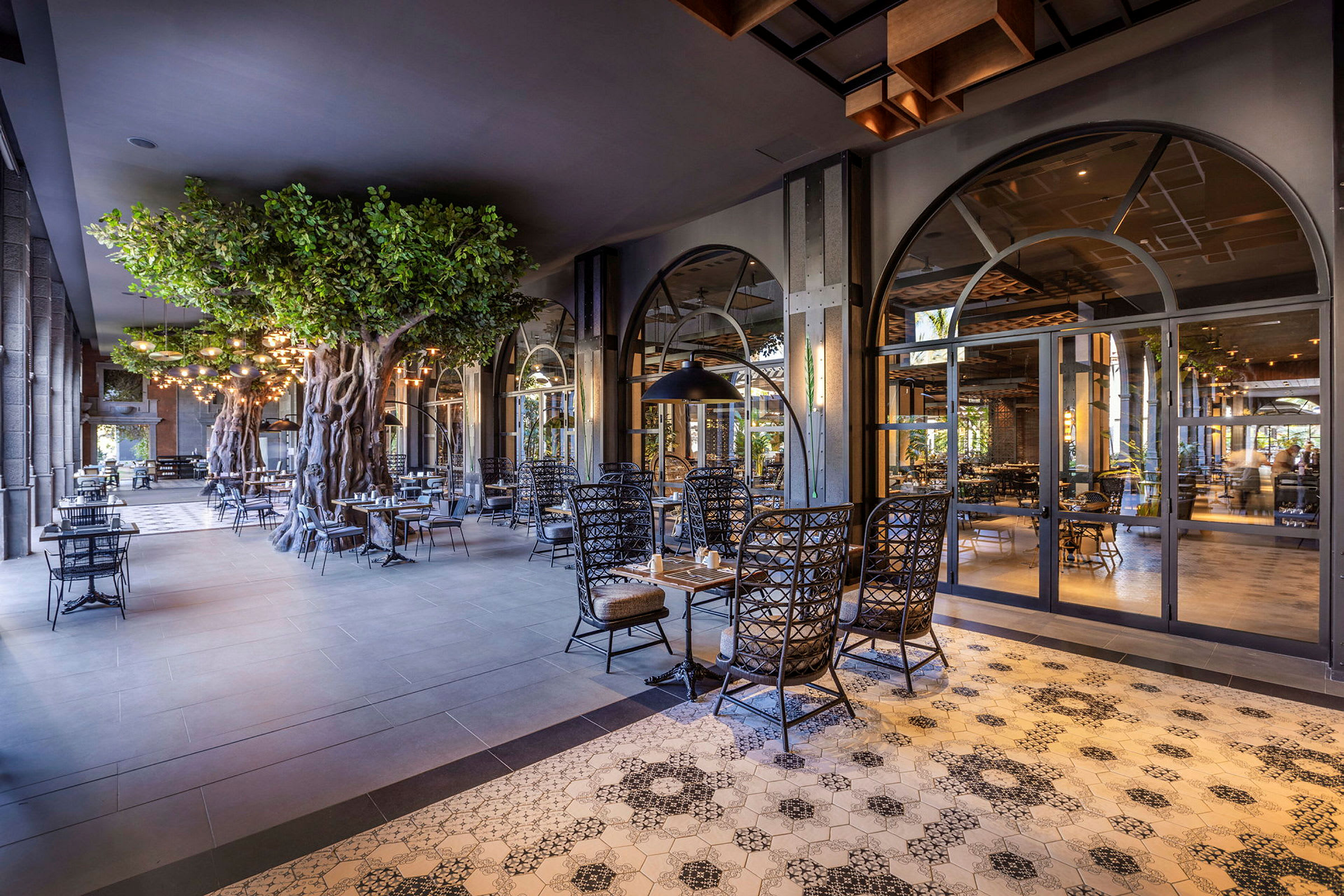 Ett elegant restaurangområde med dekorerade kakelgolv, upplysta taklampor och konstgjorda träd som bidrar till en stämningsfull atmosfär. (AI-genererad text)