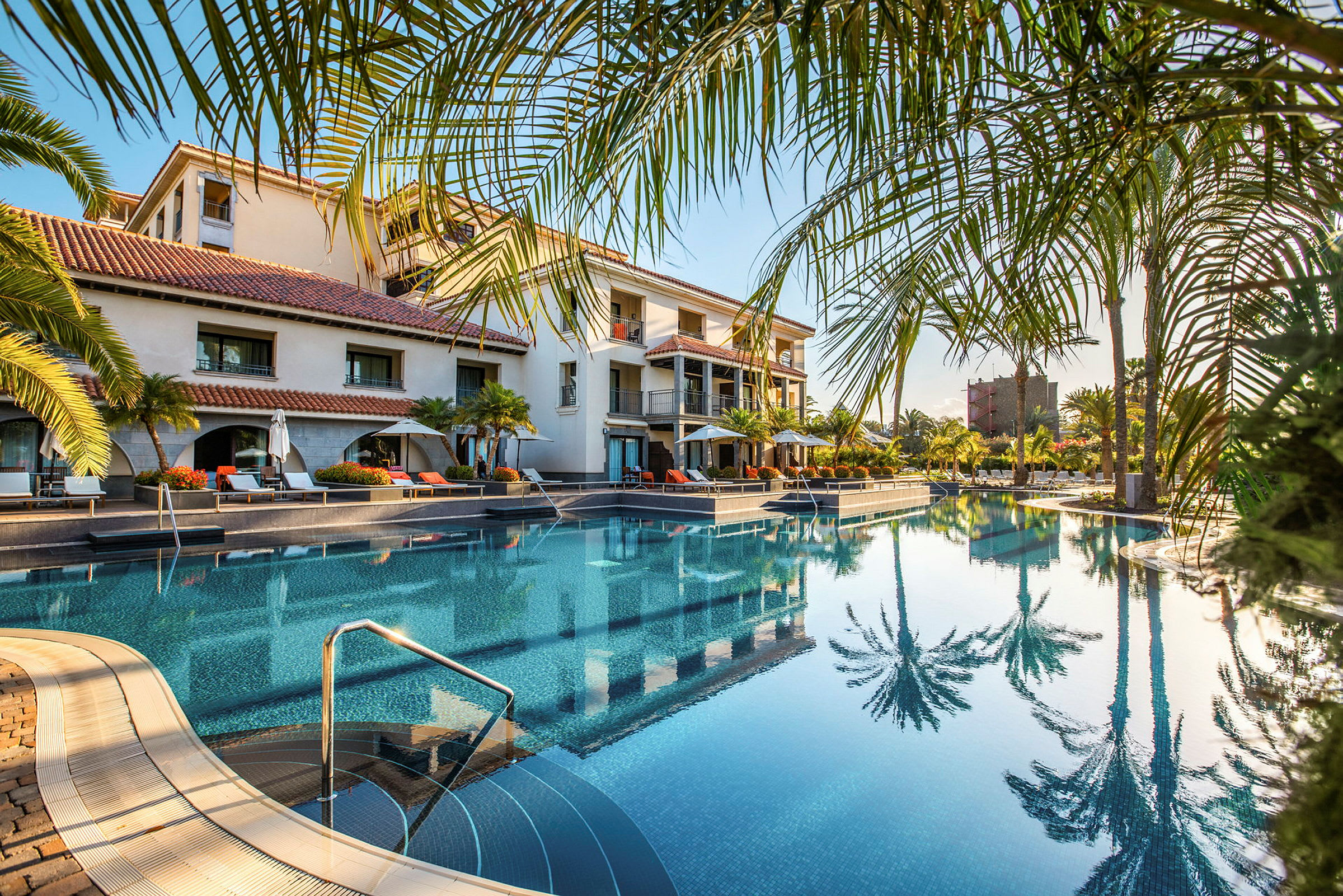 En hotellpool omgiven av palmer och solstolar. (AI-genererad text)