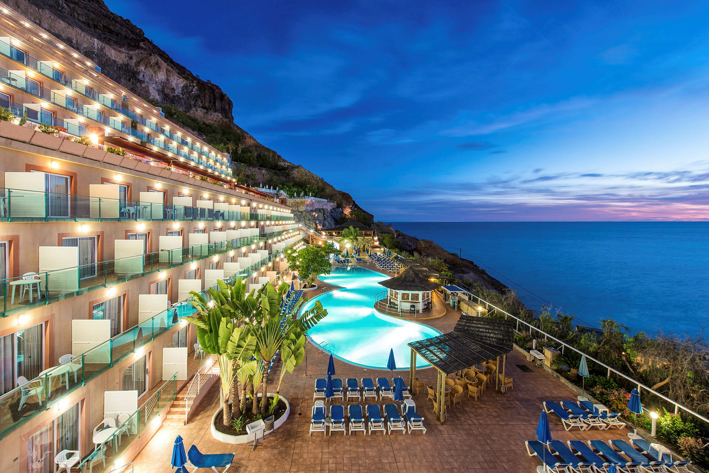 Hotellområde med pool och solstolar vid havet under kvällstid. (AI-genererad text)