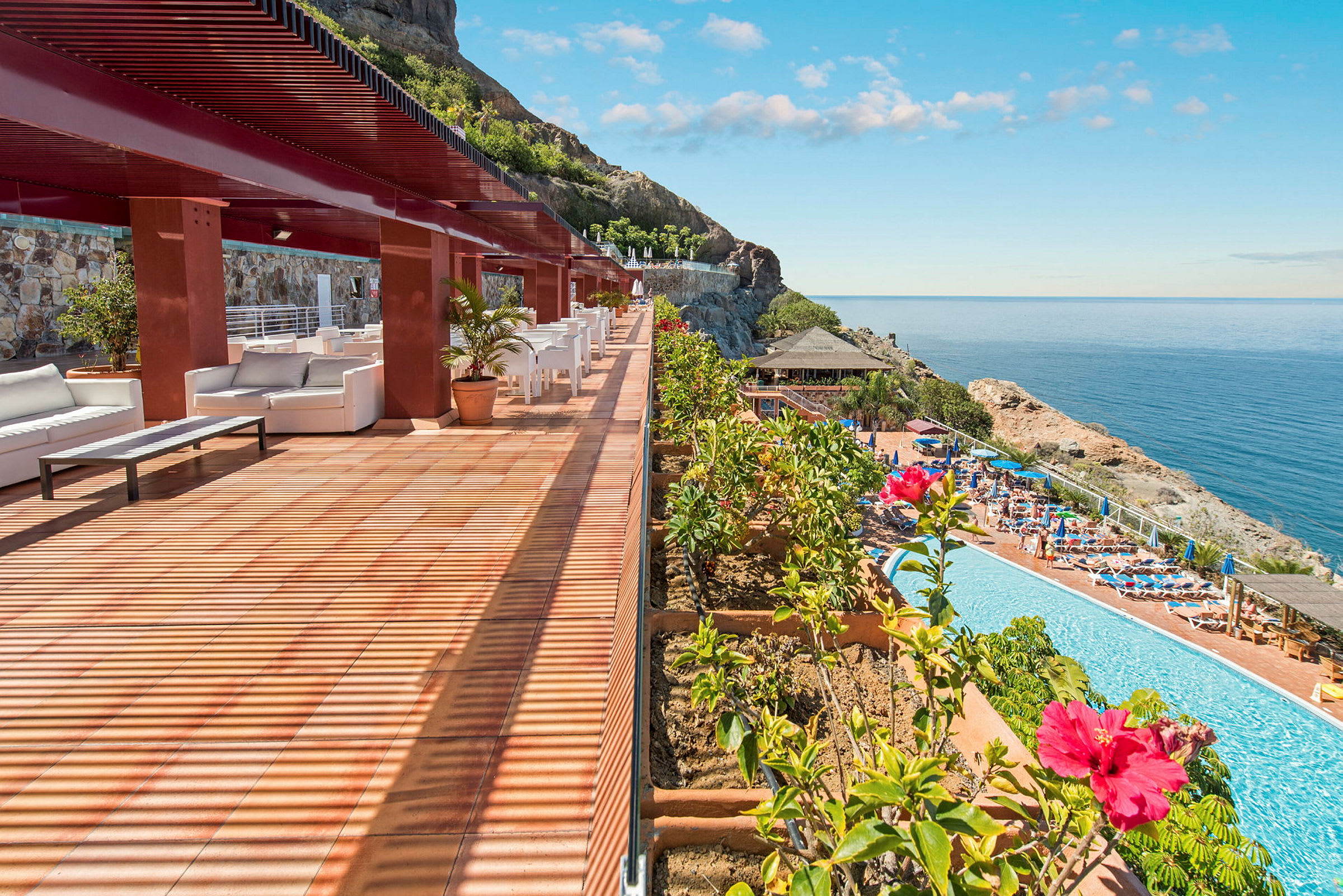 En terrass med sittplatser och utsikt över en pool och havet. (AI-genererad text)