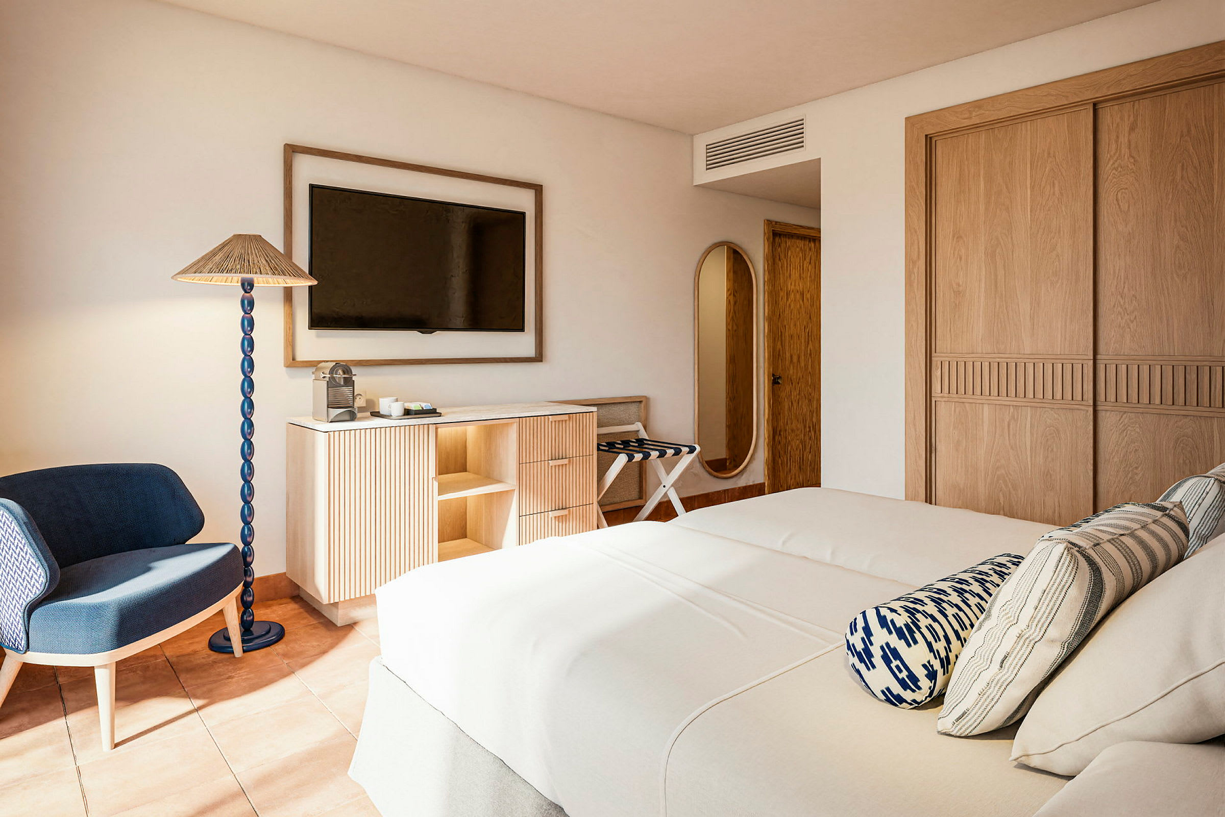 Ett hotellrum med två sängar, en TV på väggen, ett modernt skåp och en stol intill en golvlampa. (AI-genererad text)
