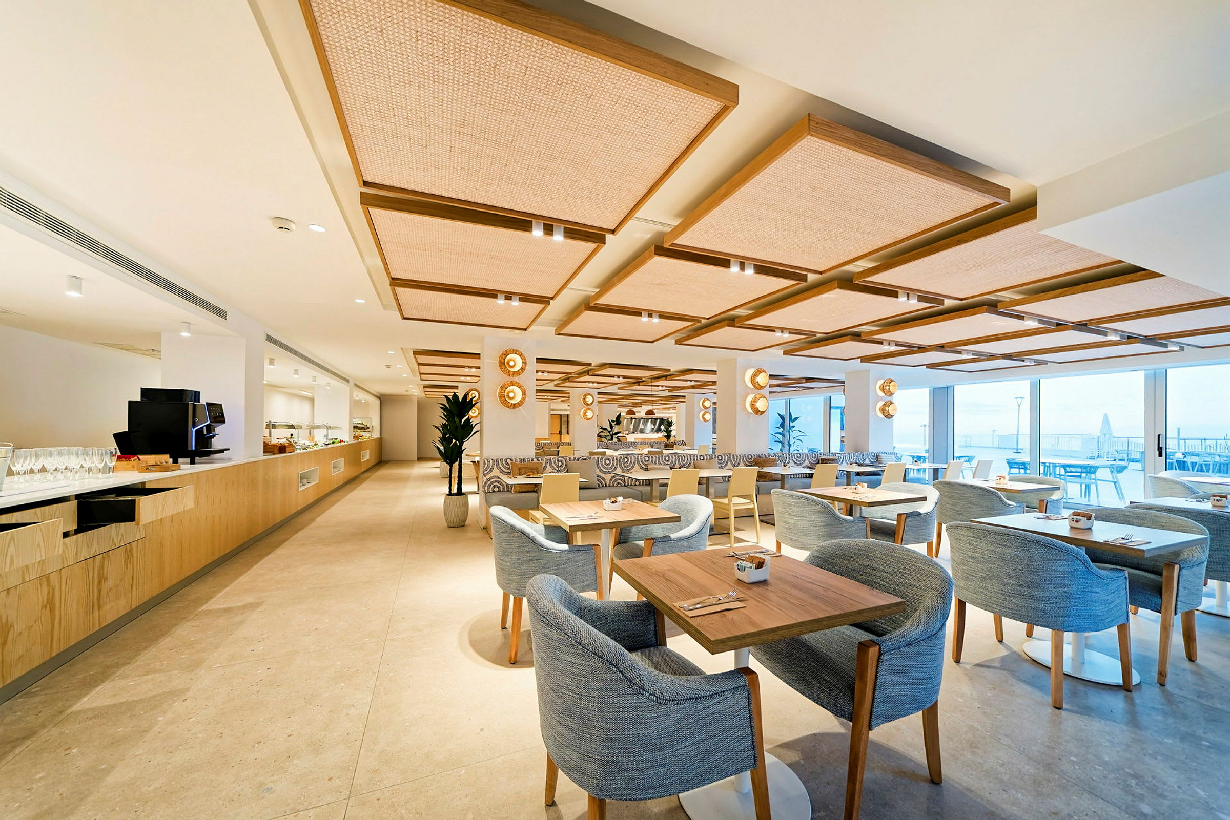 En modern restaurang med ljus inredning, bord och stolar samt stora fönster med utsikt. (AI-genererad text)