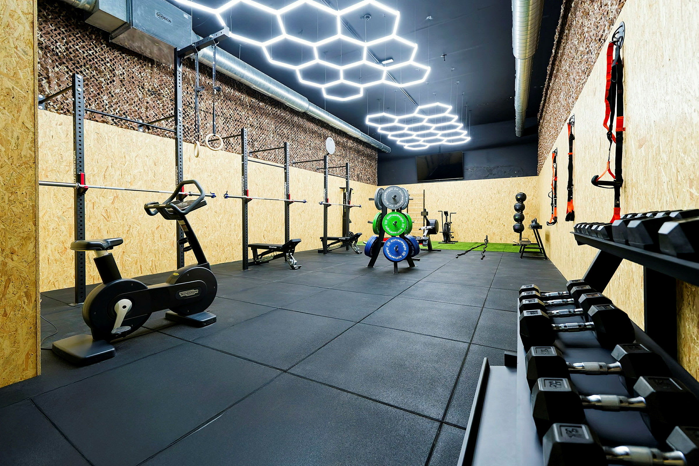 Bild av ett gym med olika träningsutrustningar såsom vikter, motionscyklar och träningsställningar. (AI-genererad text)