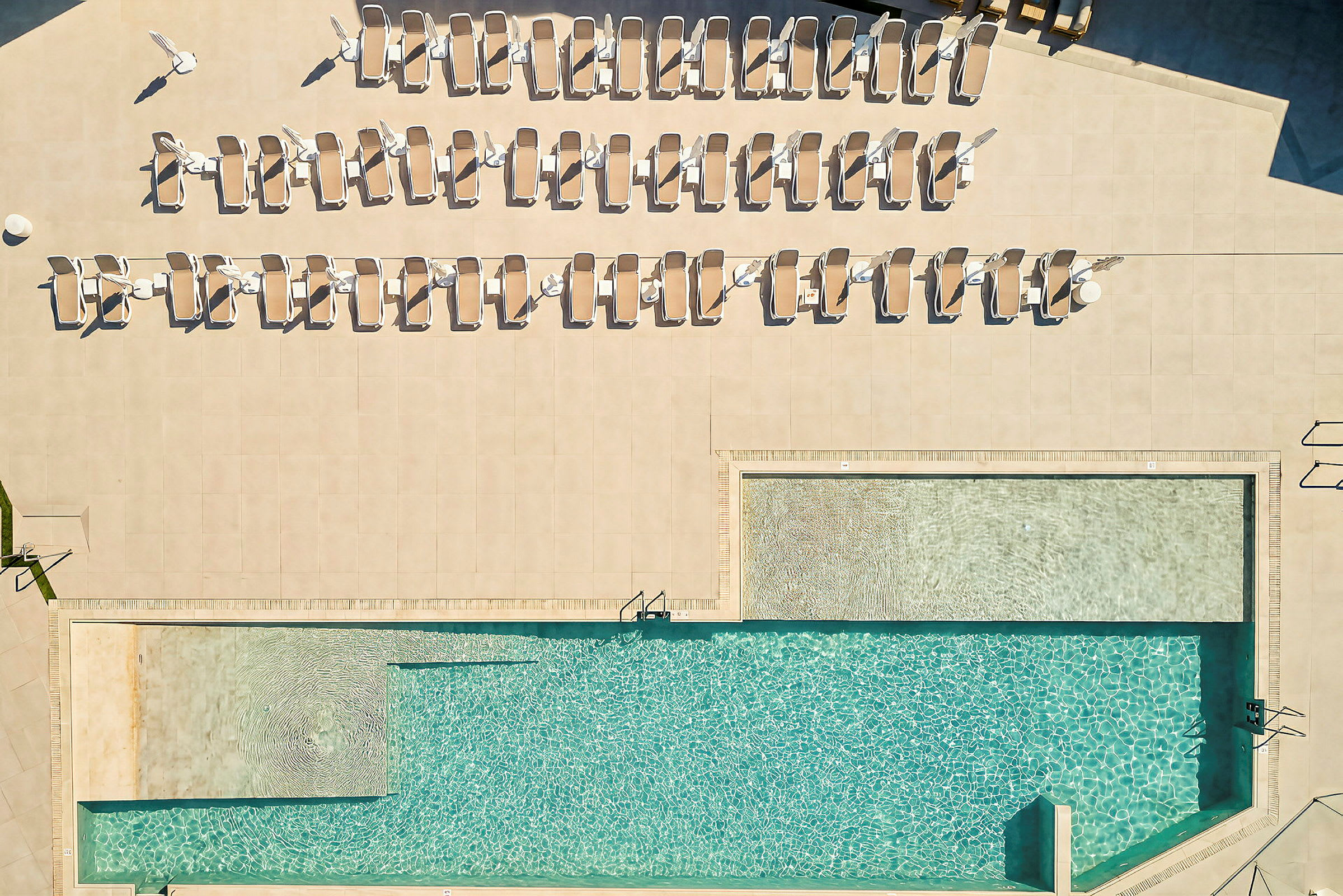 Vy ovanifrån av en pool med solstolar runt omkring. (AI-genererad text)