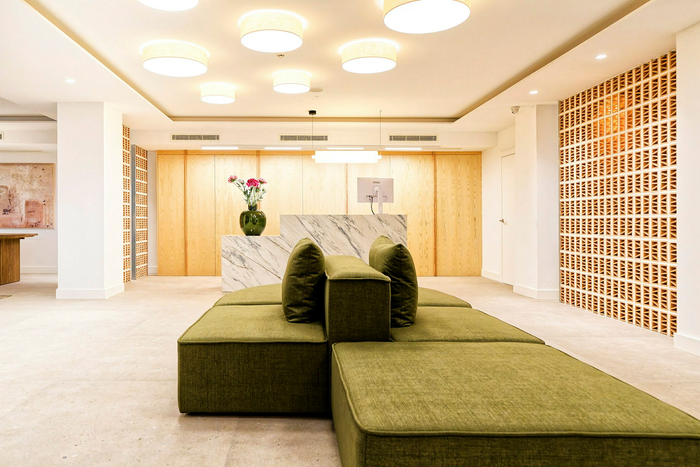 En modern reception med marmordisk, gröna sittmöbler och dekorativa träluckor. (AI-genererad text)