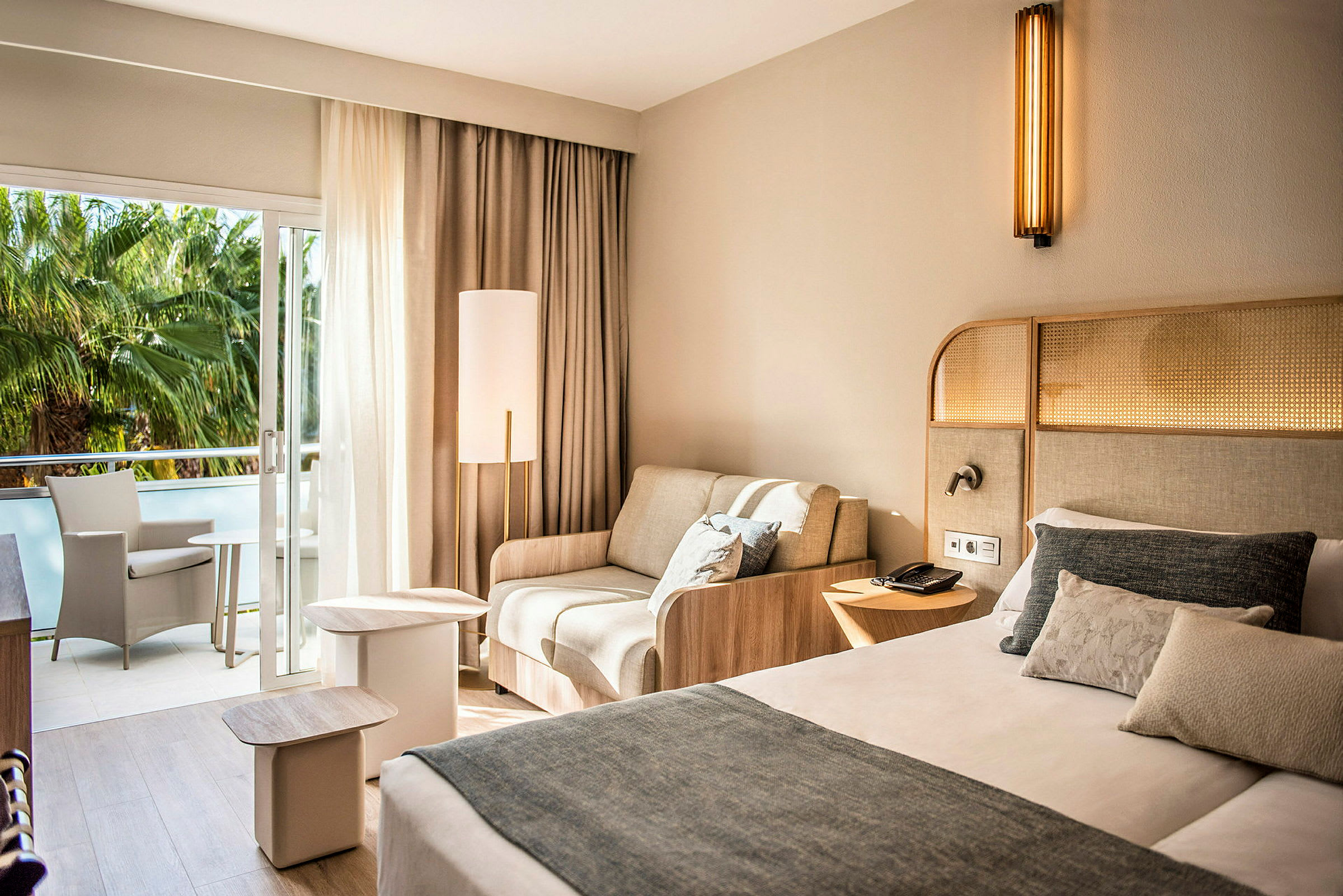 Ett hotellrum med en säng, en soffa och en balkong med sittmöbler. (AI-genererad text)