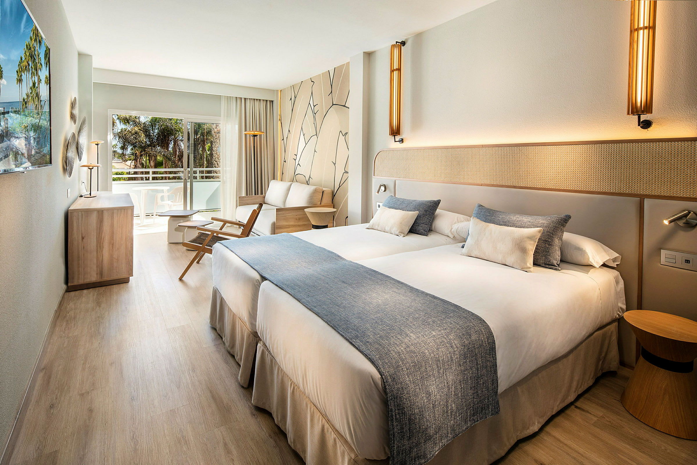 Ett hotellrum med två enkelsängar, sittmöbler och en balkong. (AI-genererad text)