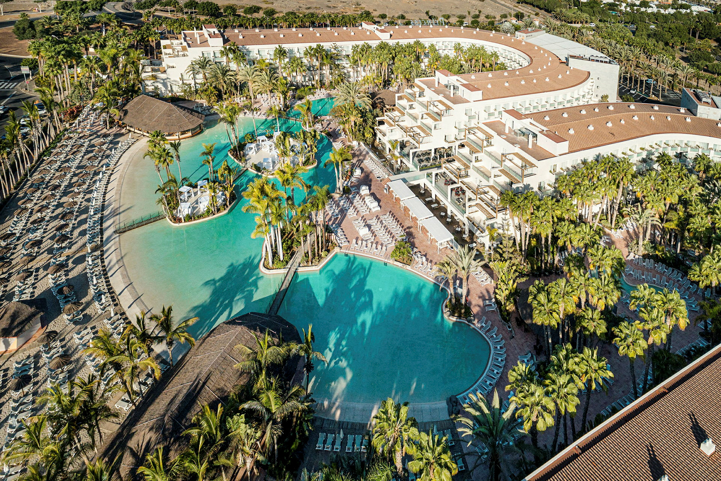 Flygvy av en resort med stora pooler, palmer och solstolar. (AI-genererad text)