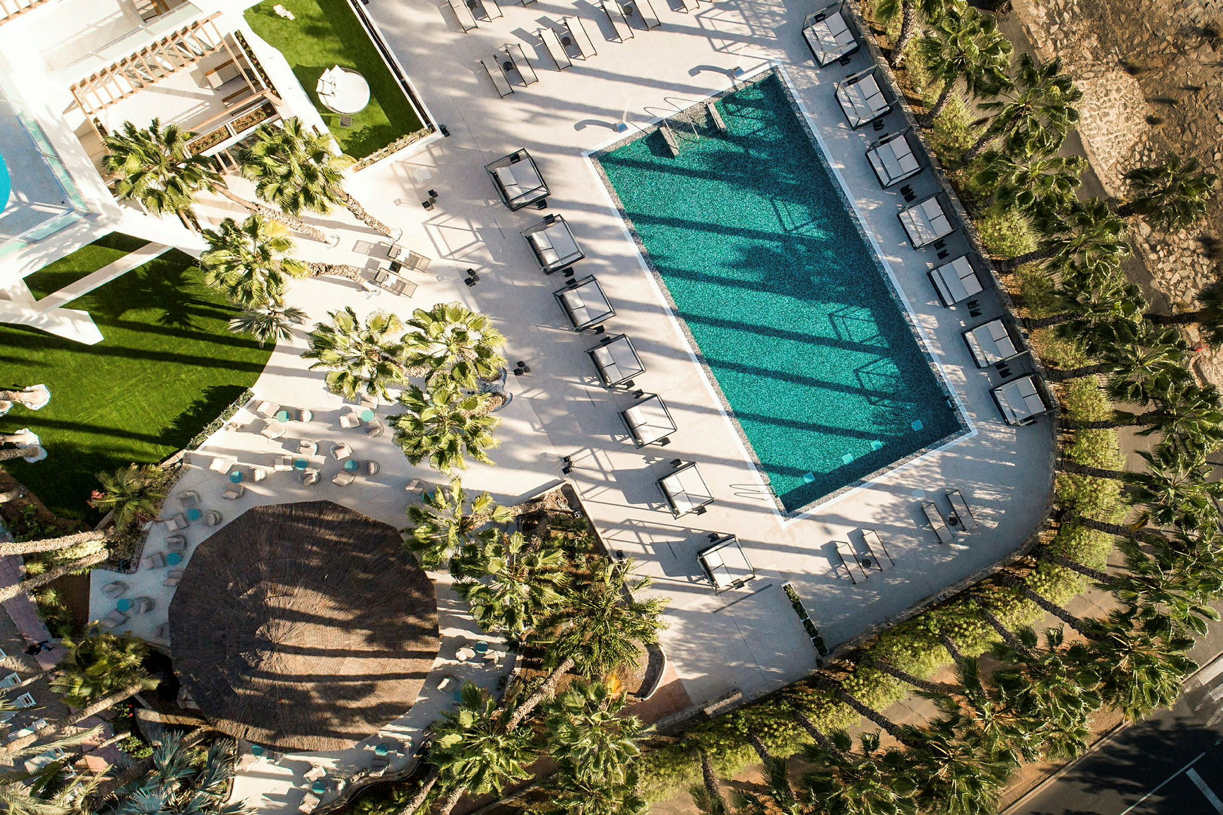 Flygfoto av en swimmingpool med solstolar och parasoller, omgiven av palmer och grönytor. (AI-genererad text)