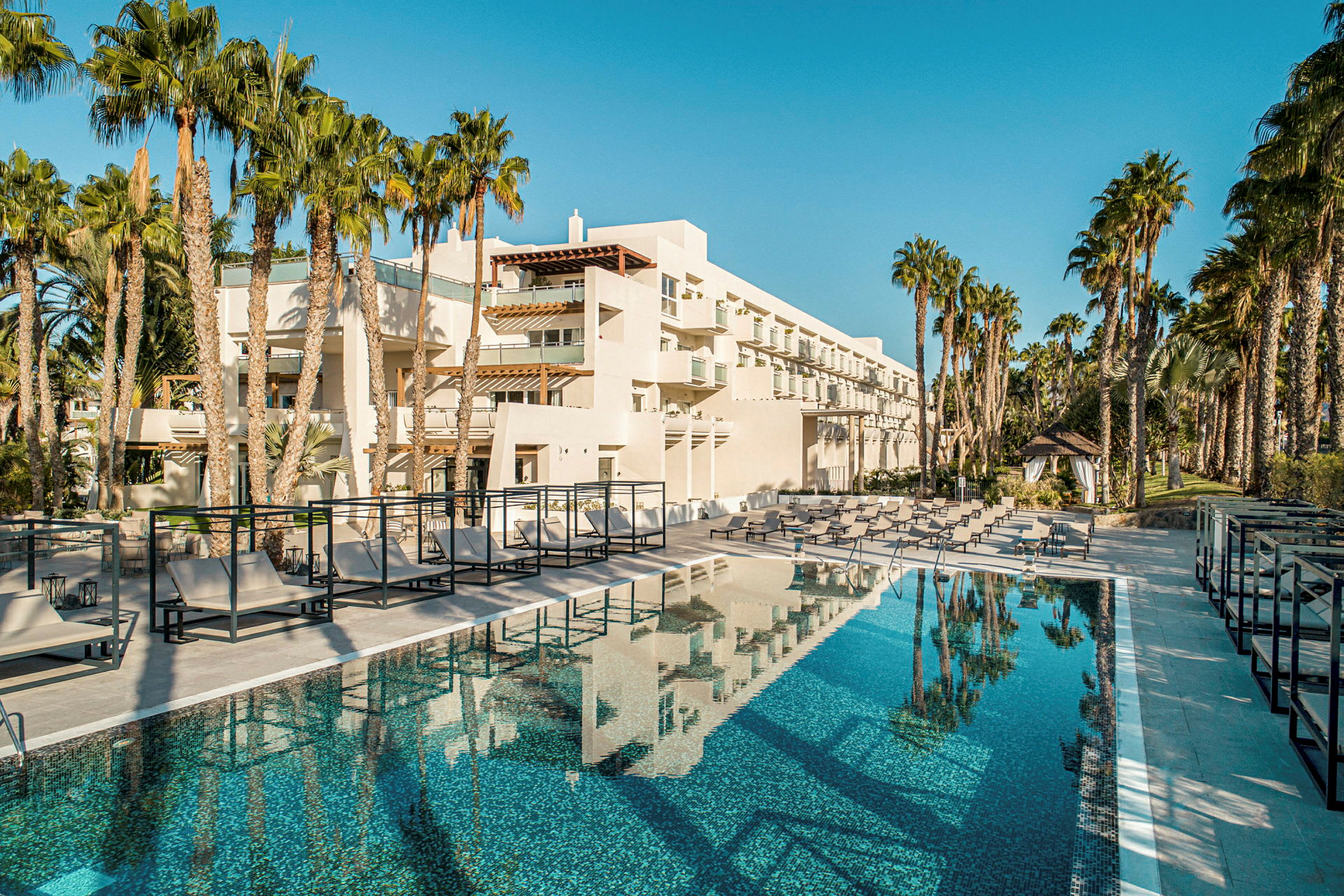 Modern hotellbyggnad med pool och omgivande palmer. (AI-genererad text)