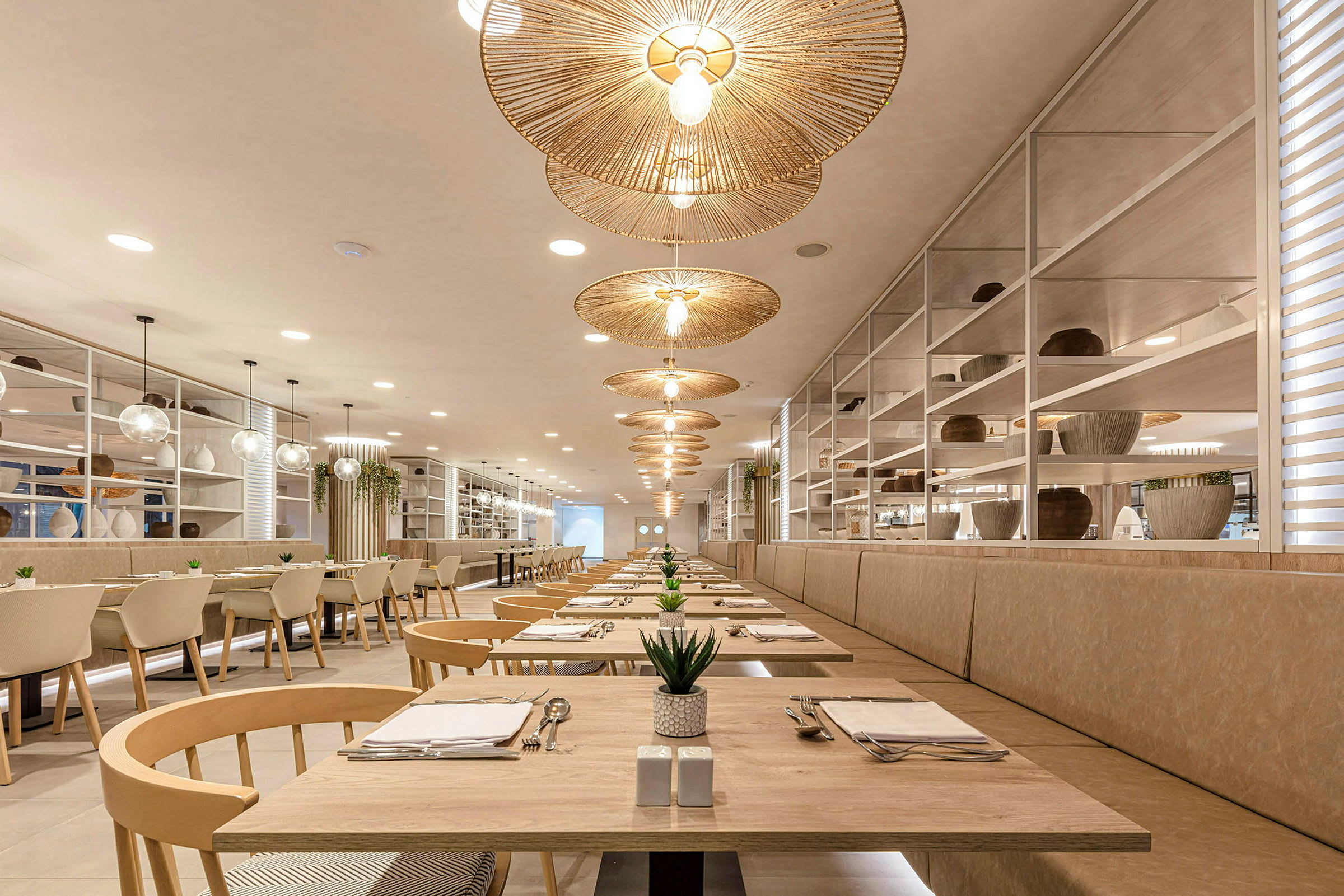 Luftig restaurang med eleganta träbord, runda rottinglampor och växtdekorationer. (AI-genererad text)