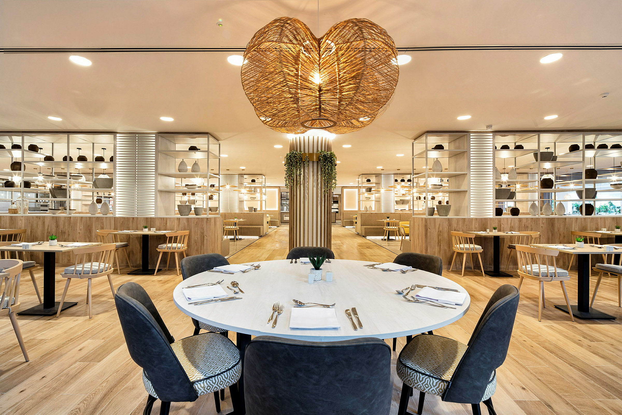 Ett modernt inrett restauranginteriör med ett runt bord i förgrunden, omgiven av sittplatser och dekorativa hyllor. (AI-genererad text)