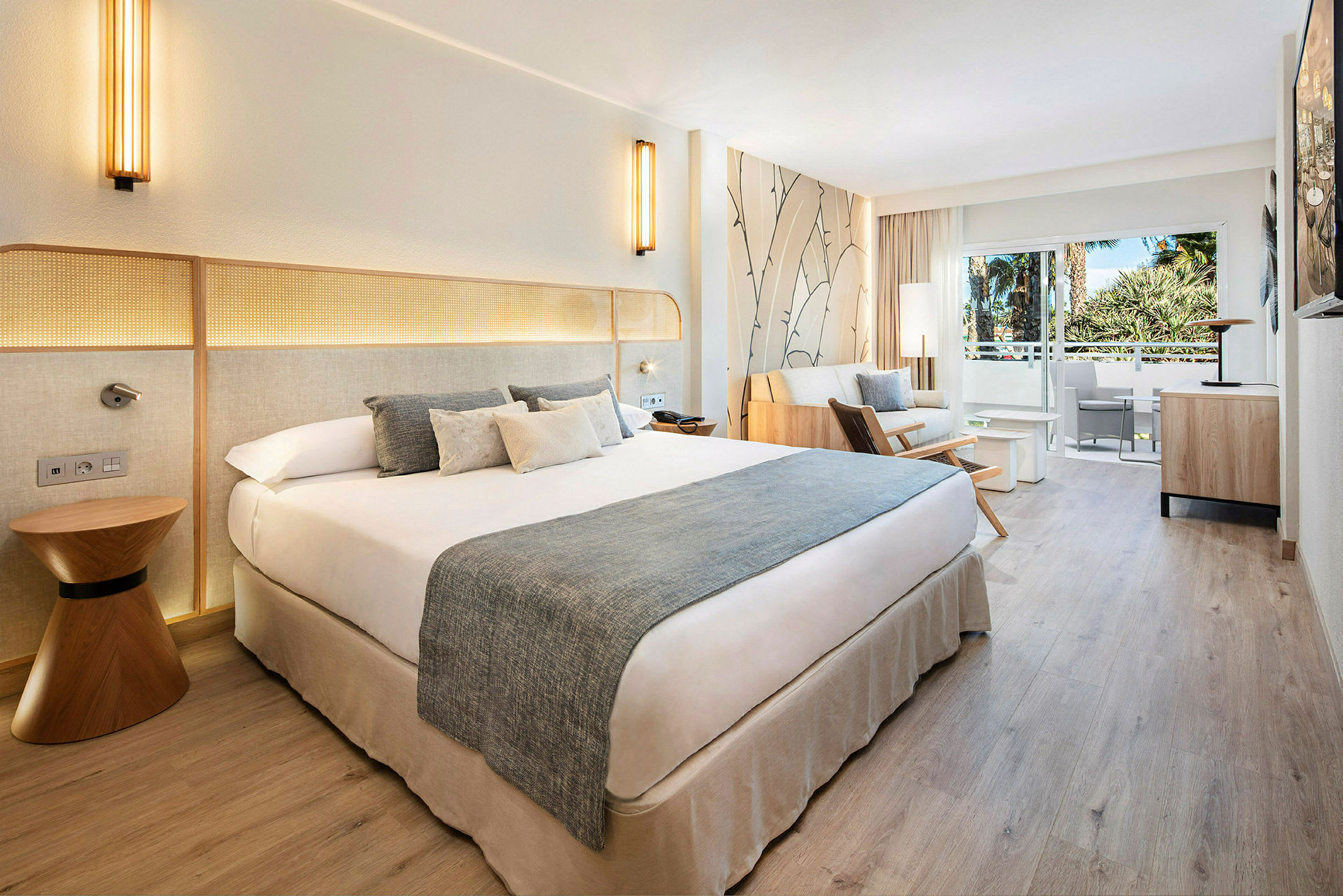 Hotellrum med dubbelsäng, soffgrupp och balkong med utsikt. (AI-genererad text)