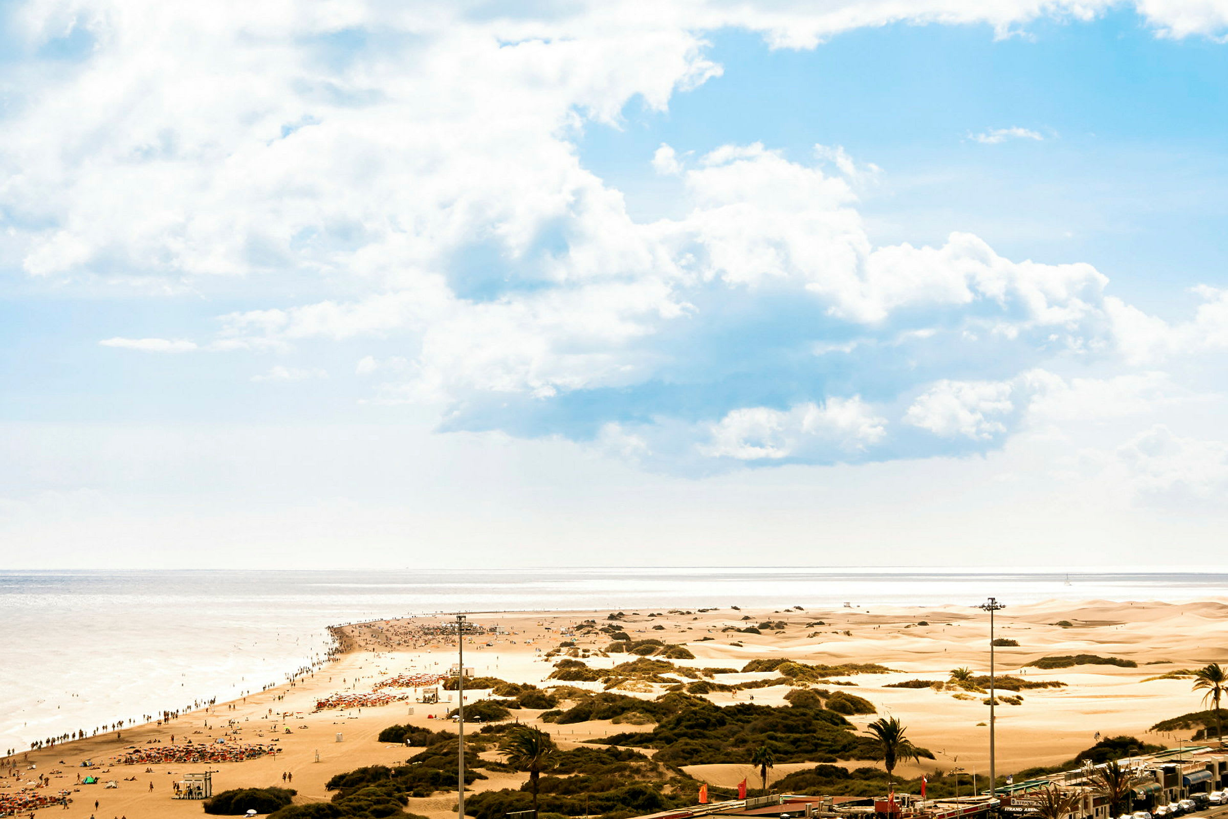 En sandstrand med människor samt sanddyner i bakgrunden under en blå himmel. (AI-genererad text)