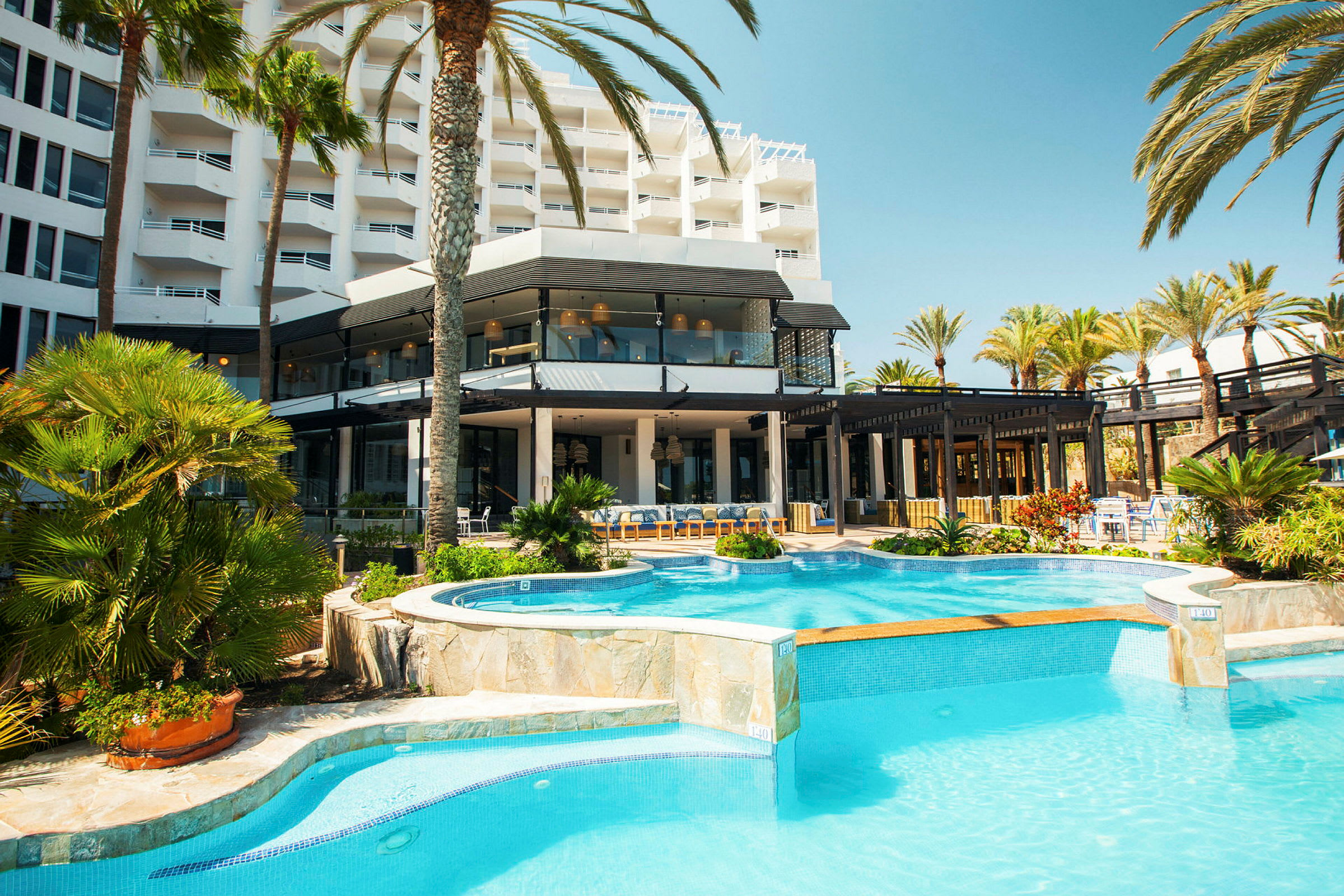 Hotellbyggnad med poolområde och omgivande palmer. (AI-genererad text)