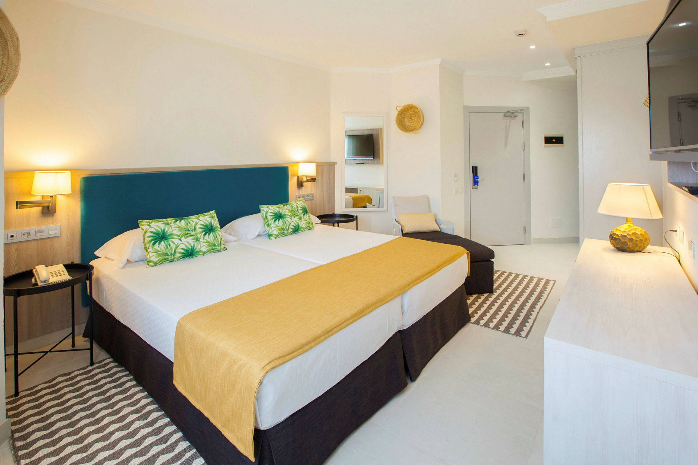Ett ljus och välmöblerat hotellrum med två sängar, en soffa och en TV. (AI-genererad text)