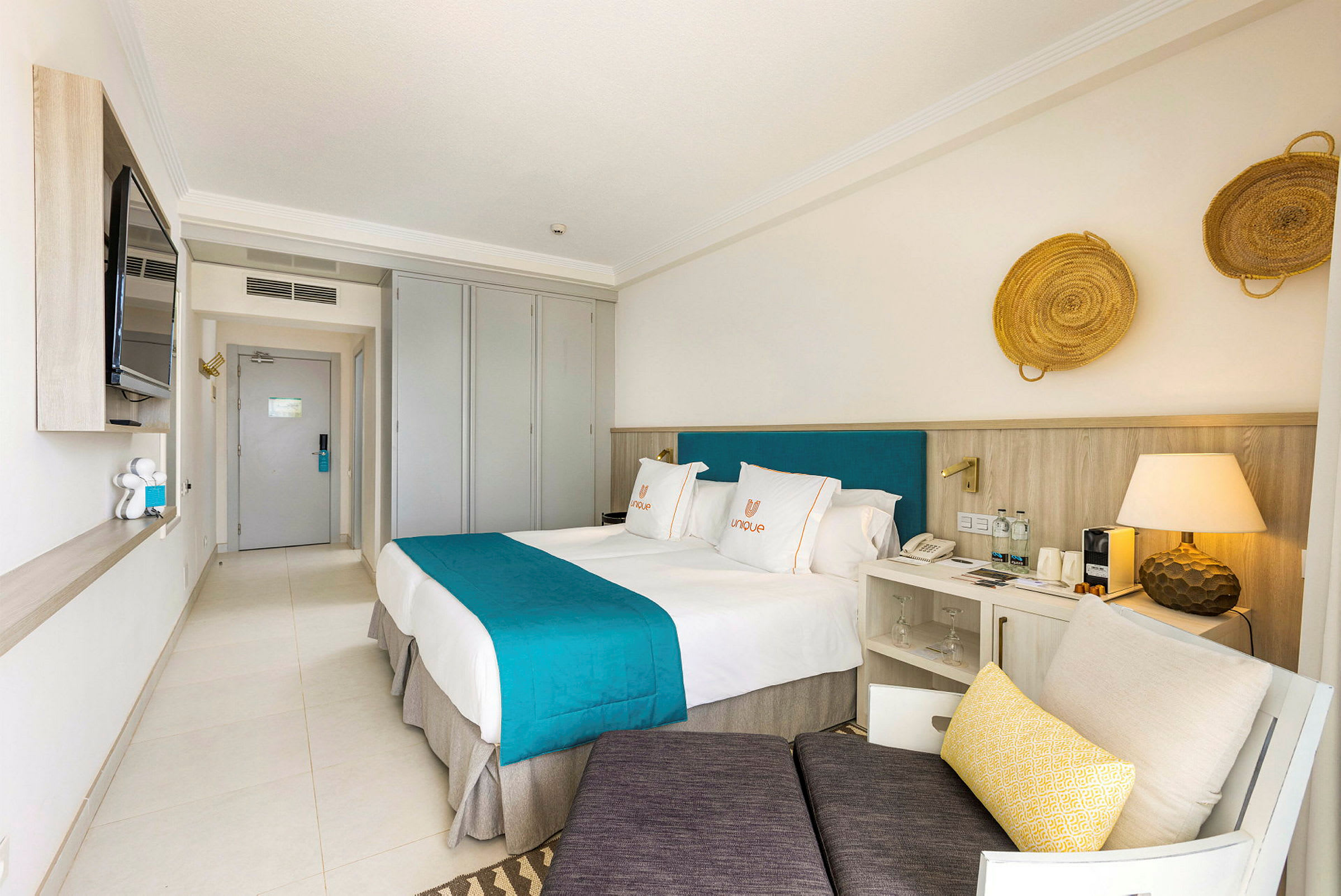 Ett hotellrum med två sängar, turkosa sängöverkast och ljus inredning. (AI-genererad text)