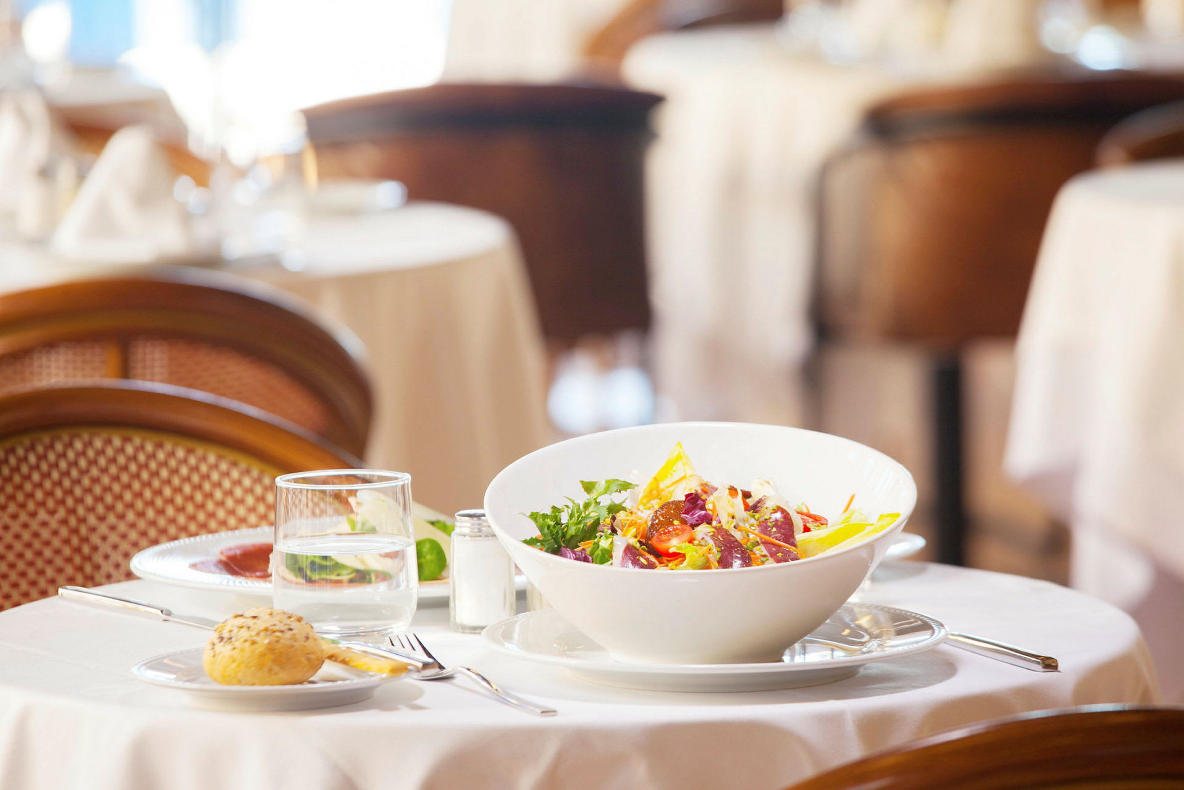 En sallad i en vit skål på ett dukat bord med glas och bestick (AI-genererad text)
