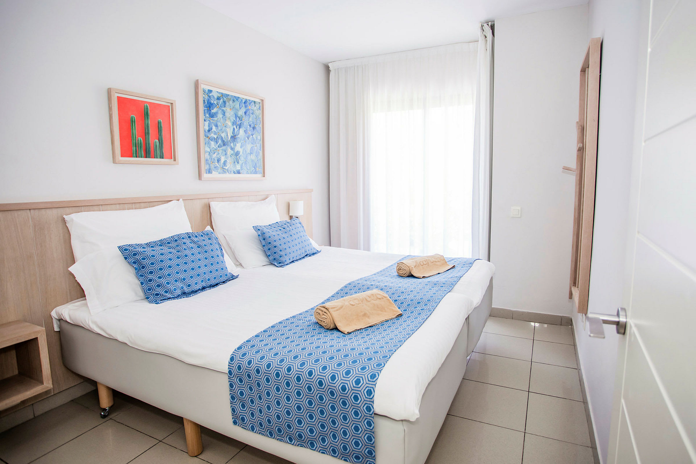 Bild på ett hotellrum med en dubbelsäng, blå detaljer och konstverk på väggen. (AI-genererad text)