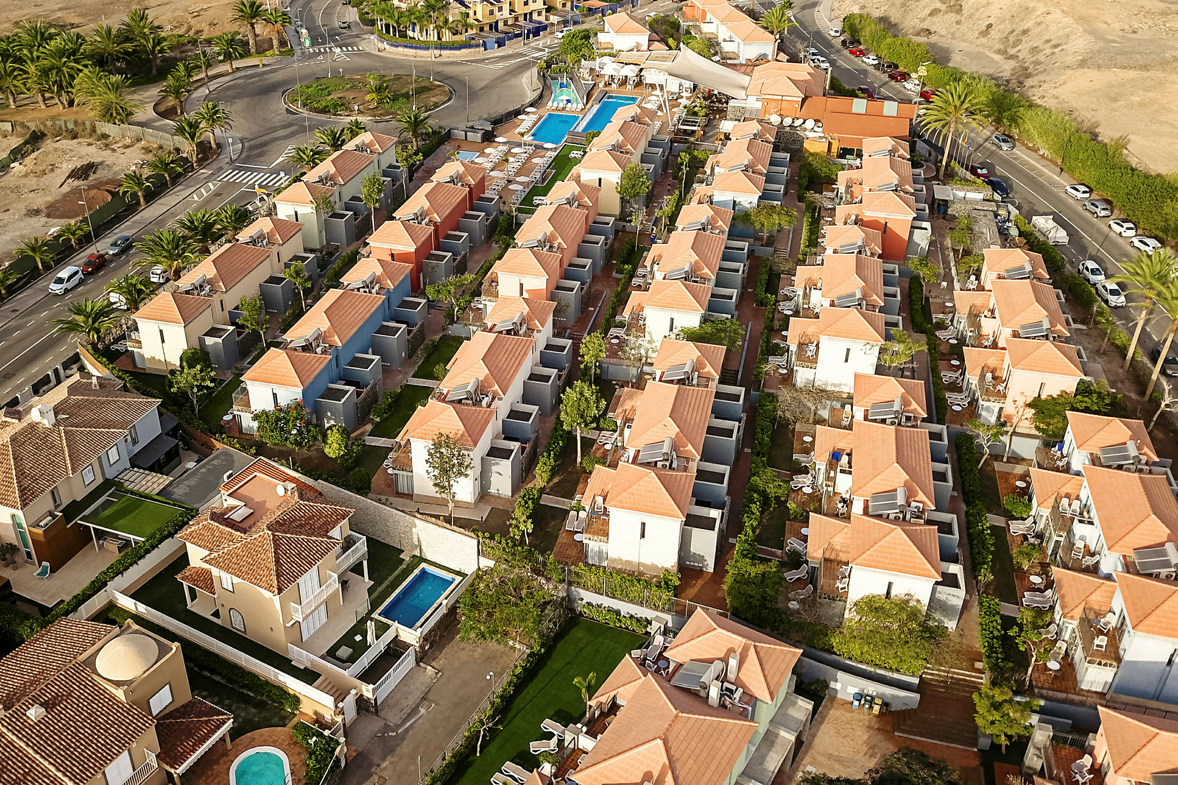 Flera hus med röda tegeltak grupperade runt en gemensam pool och grönområden. (AI-genererad text)