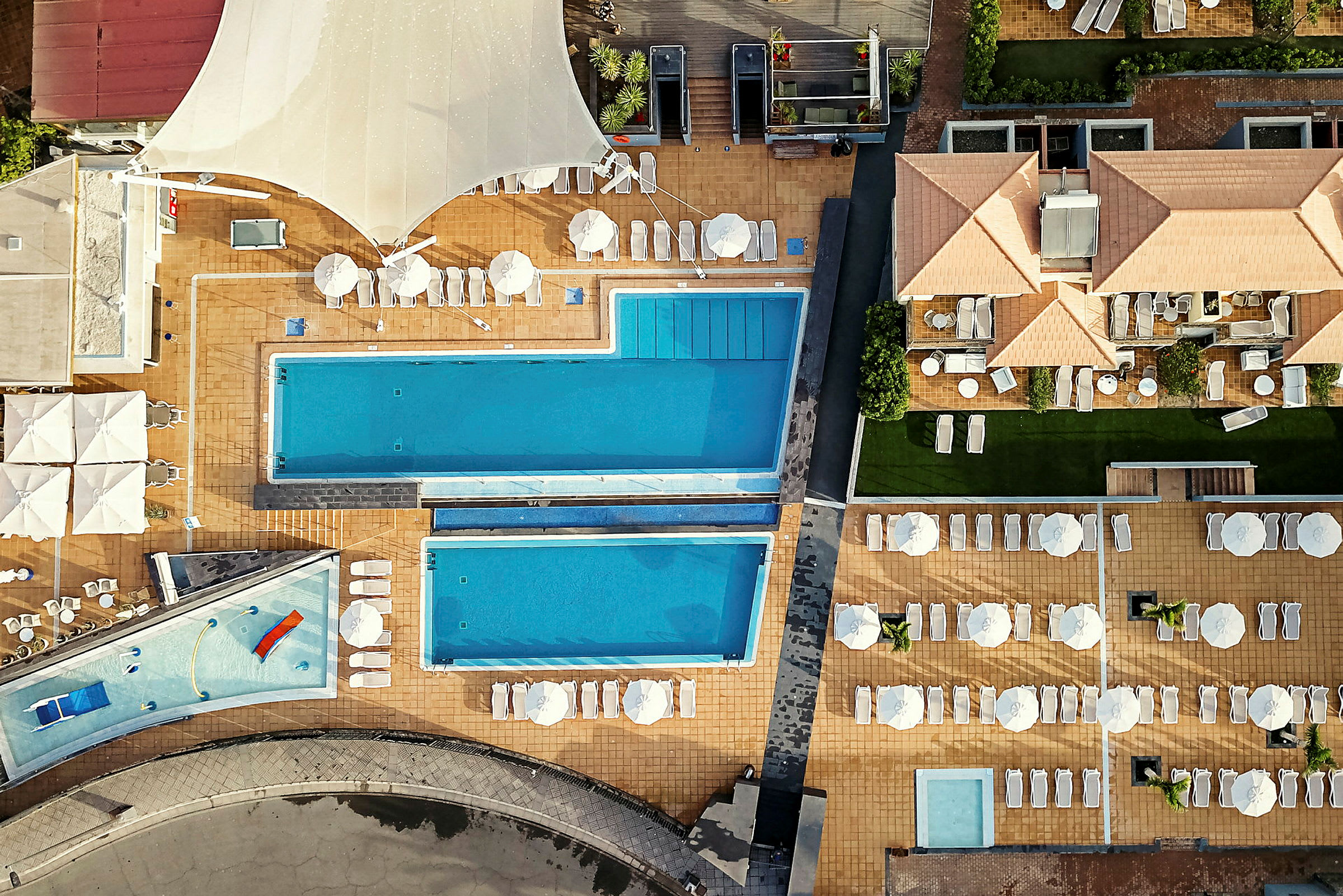 Flygbild av hotellområde med pooler och solstolar. (AI-genererad text)