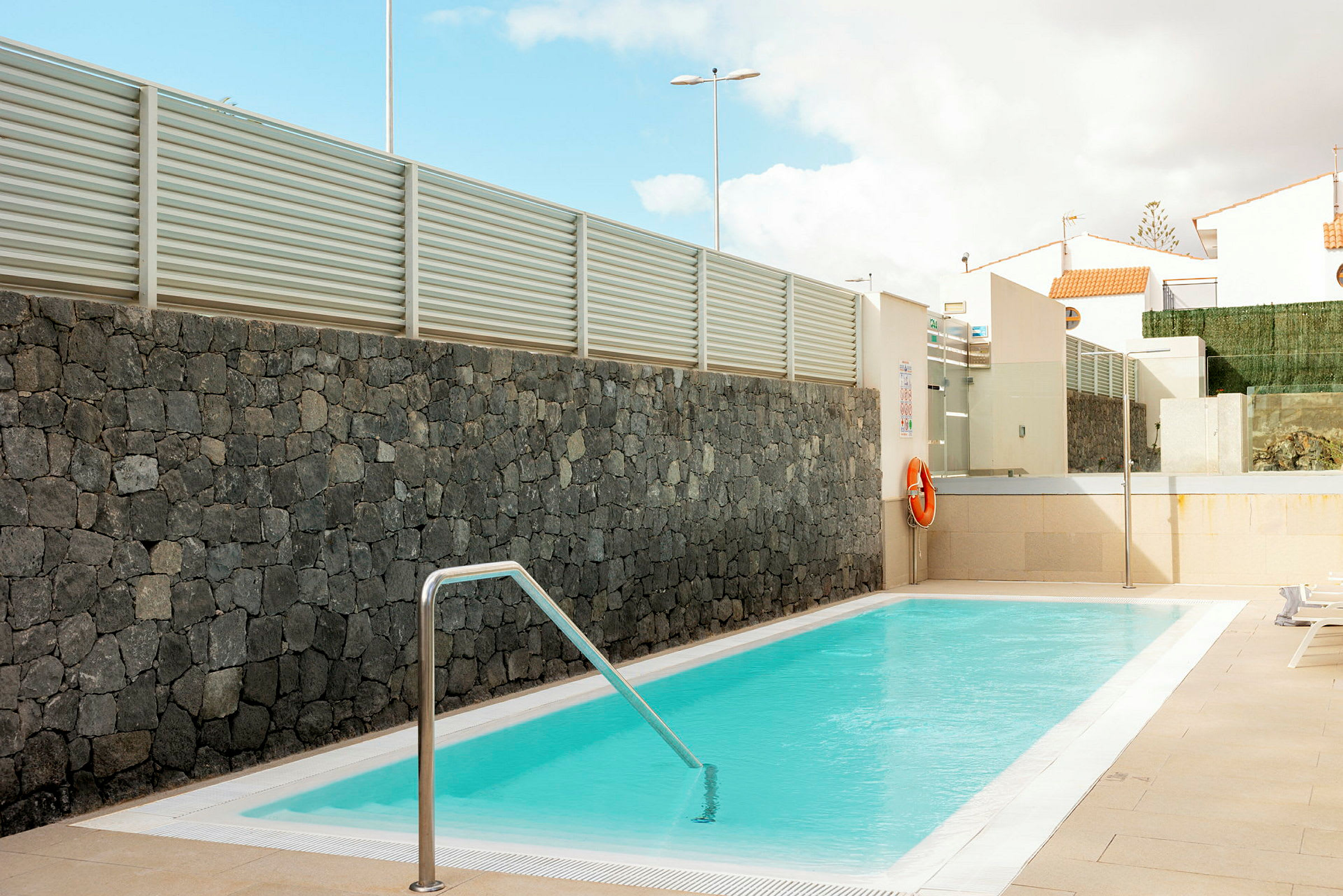 En utomhuspool med klart vatten omgiven av stenvägg och modern arkitektur. (AI-genererad text)