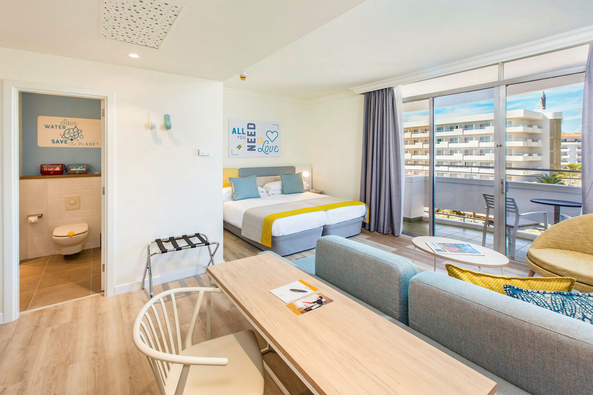 Ett hotellrum med dubbelsäng, soffgrupp och en balkong med utsikt. (AI-genererad text)