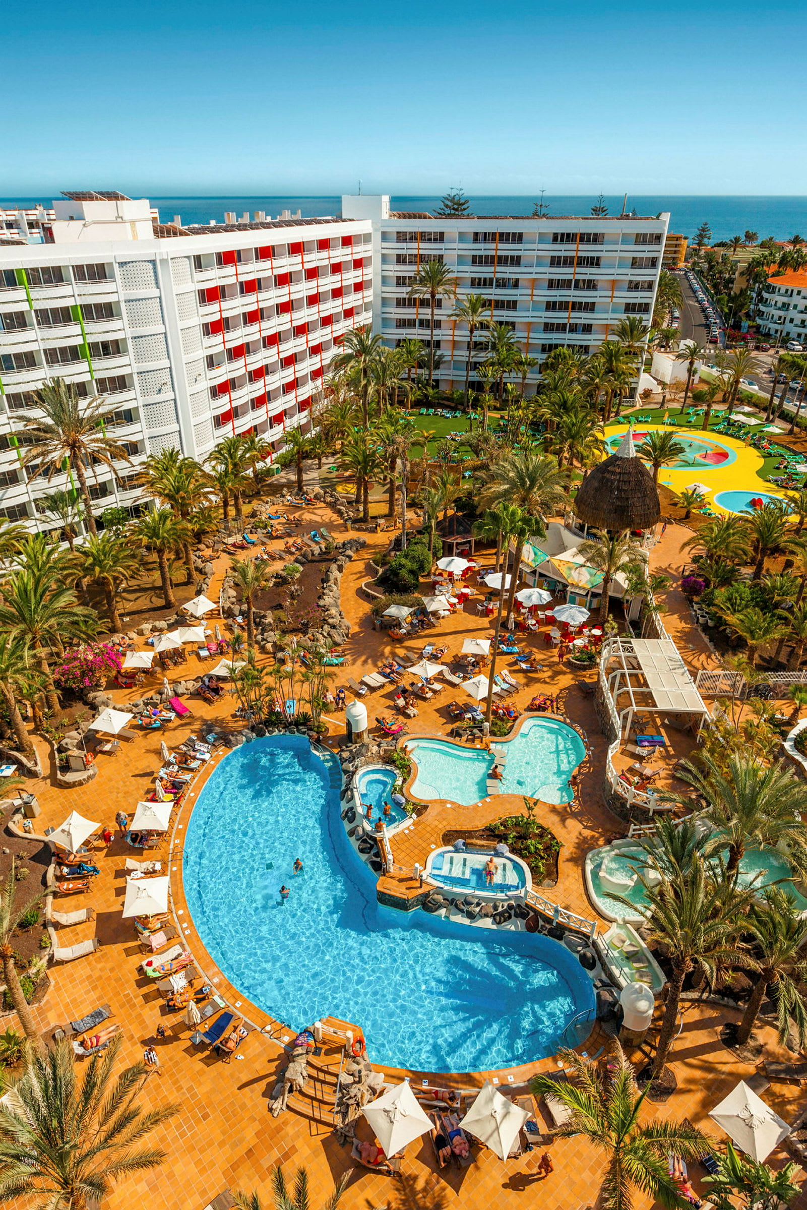 Utsikt över ett hotellområde med vita byggnader, swimmingpooler och palmer. (AI-genererad text)
