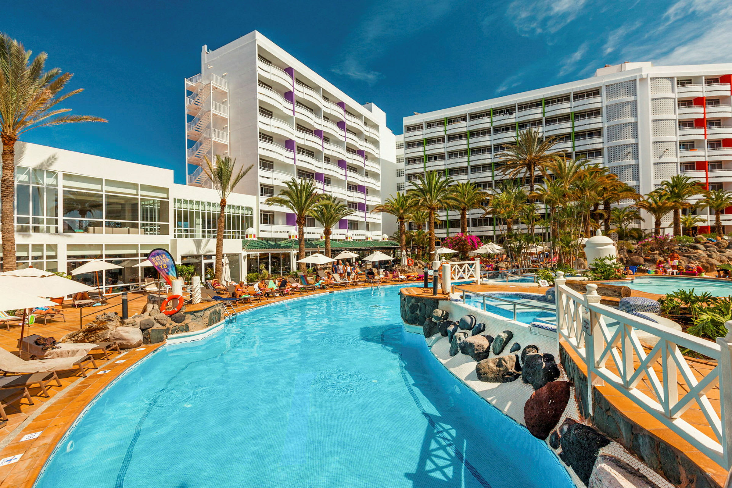 Bild av hotellområde med pool, omgivande solsängar och palmer. (AI-genererad text)