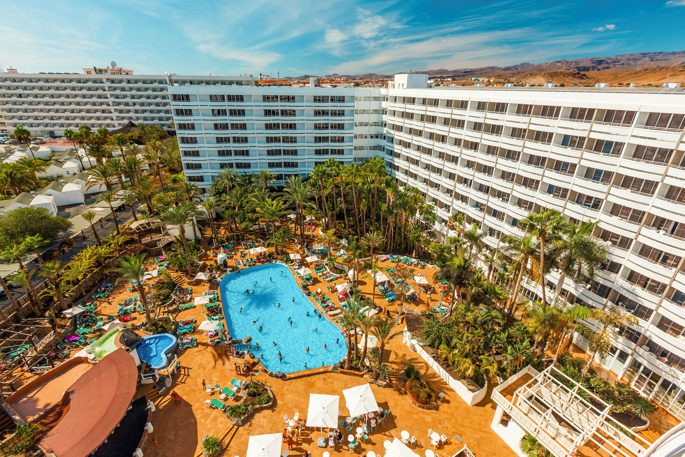 Hotellområde med stor byggnad, palmer och swimmingpool. (AI-genererad text)