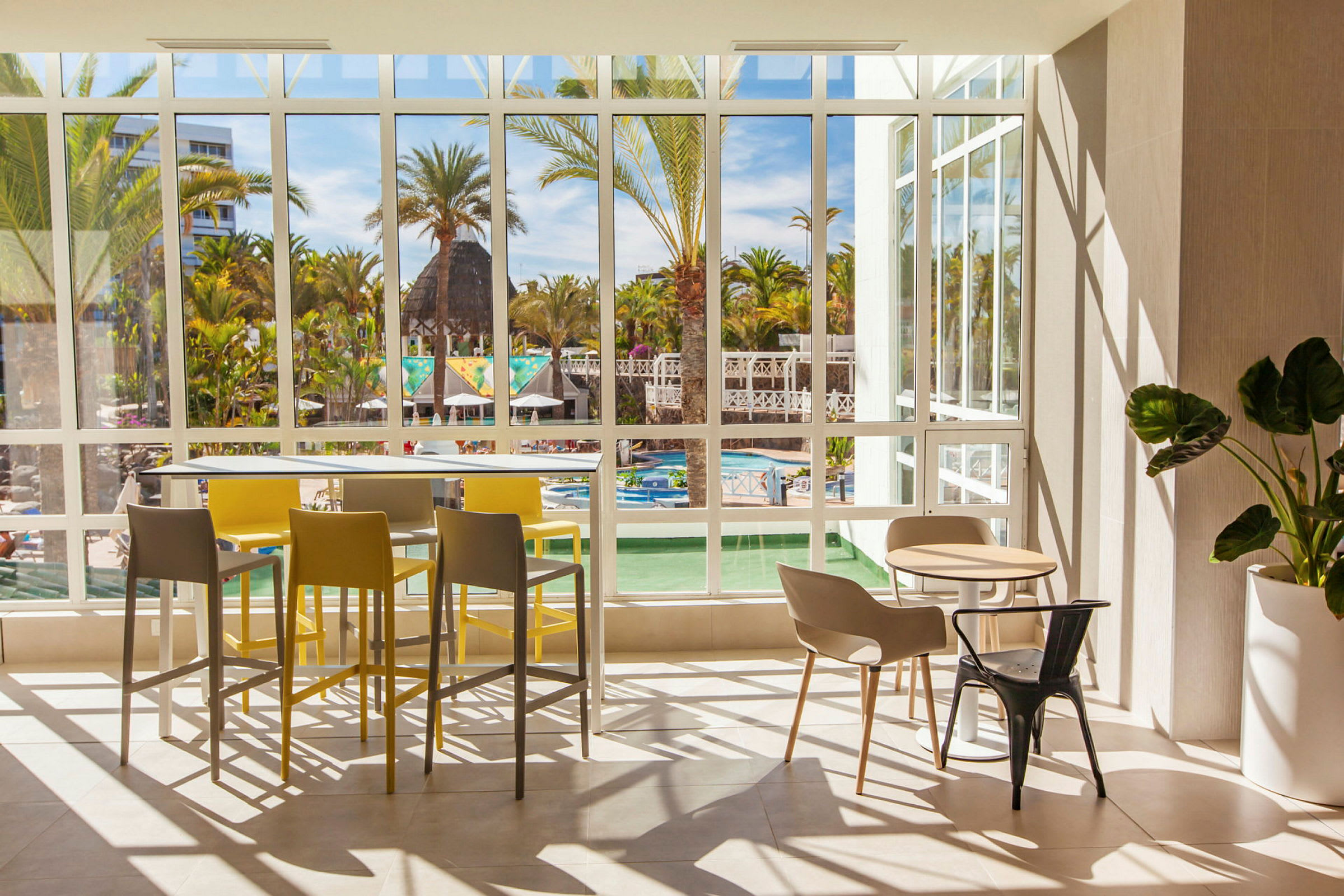 Vy från en ljus restaurang med stora fönster ut mot en pool och grönska. (AI-genererad text)