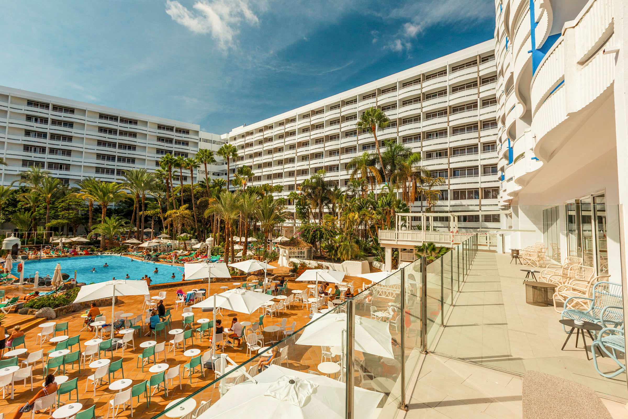 En hotellbyggnad med en stor utomhuspool omgiven av solstolar och parasoller. (AI-genererad text)