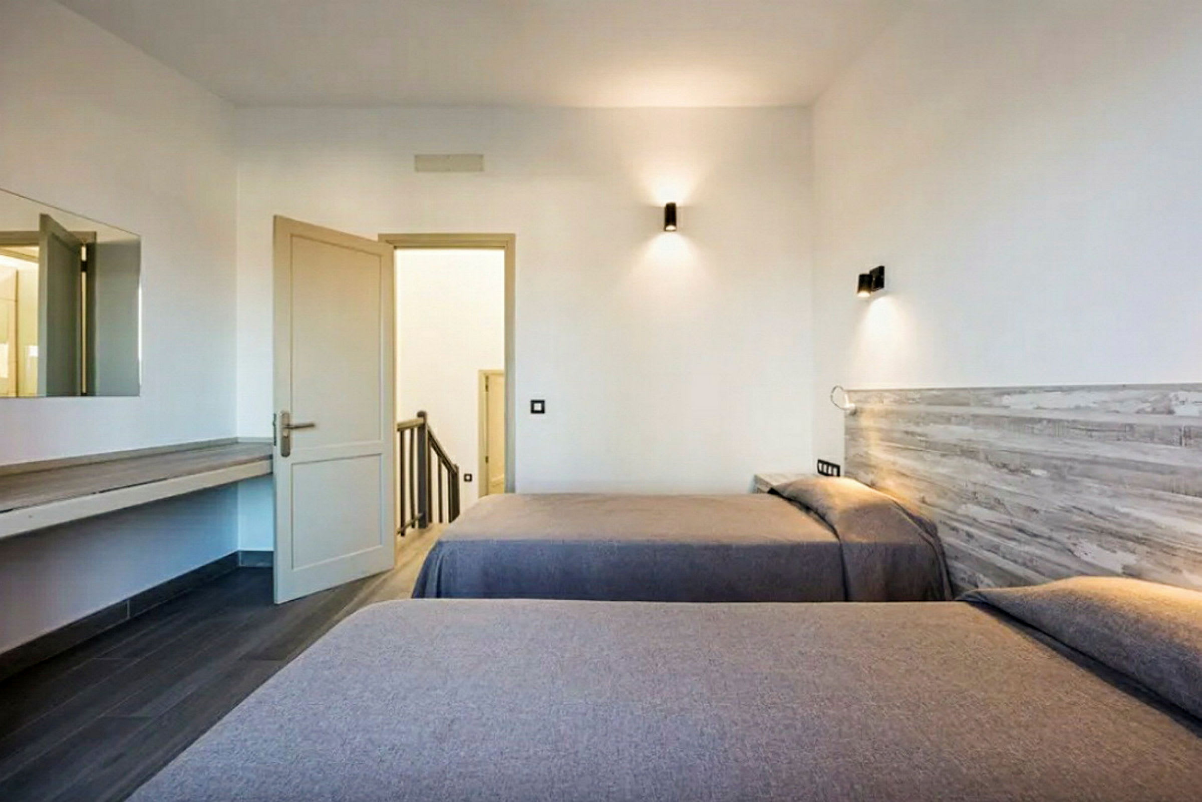 Hotellrum med två enkelsängar och en öppen dörr som leder till ett trapphus. (AI-genererad text)
