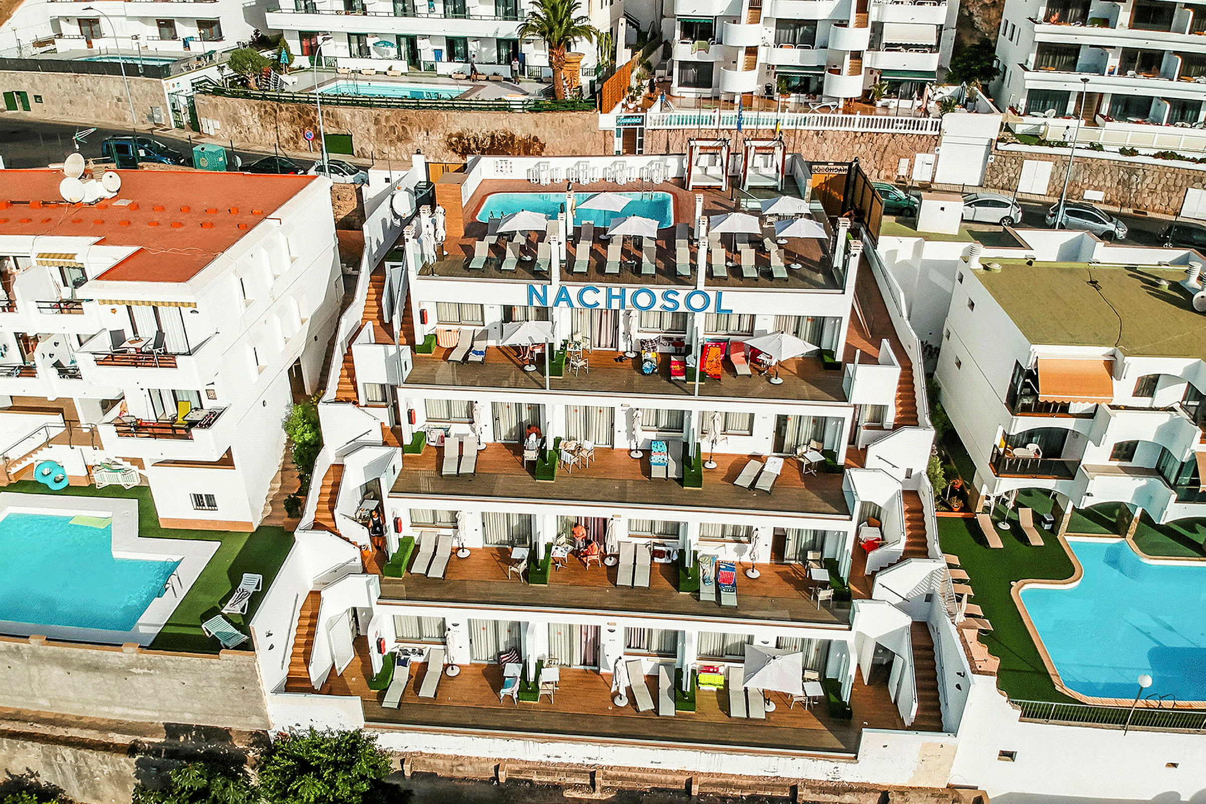 Hotell Nachosol med pool och balkonger, omgiven av andra byggnader. (AI-genererad text)