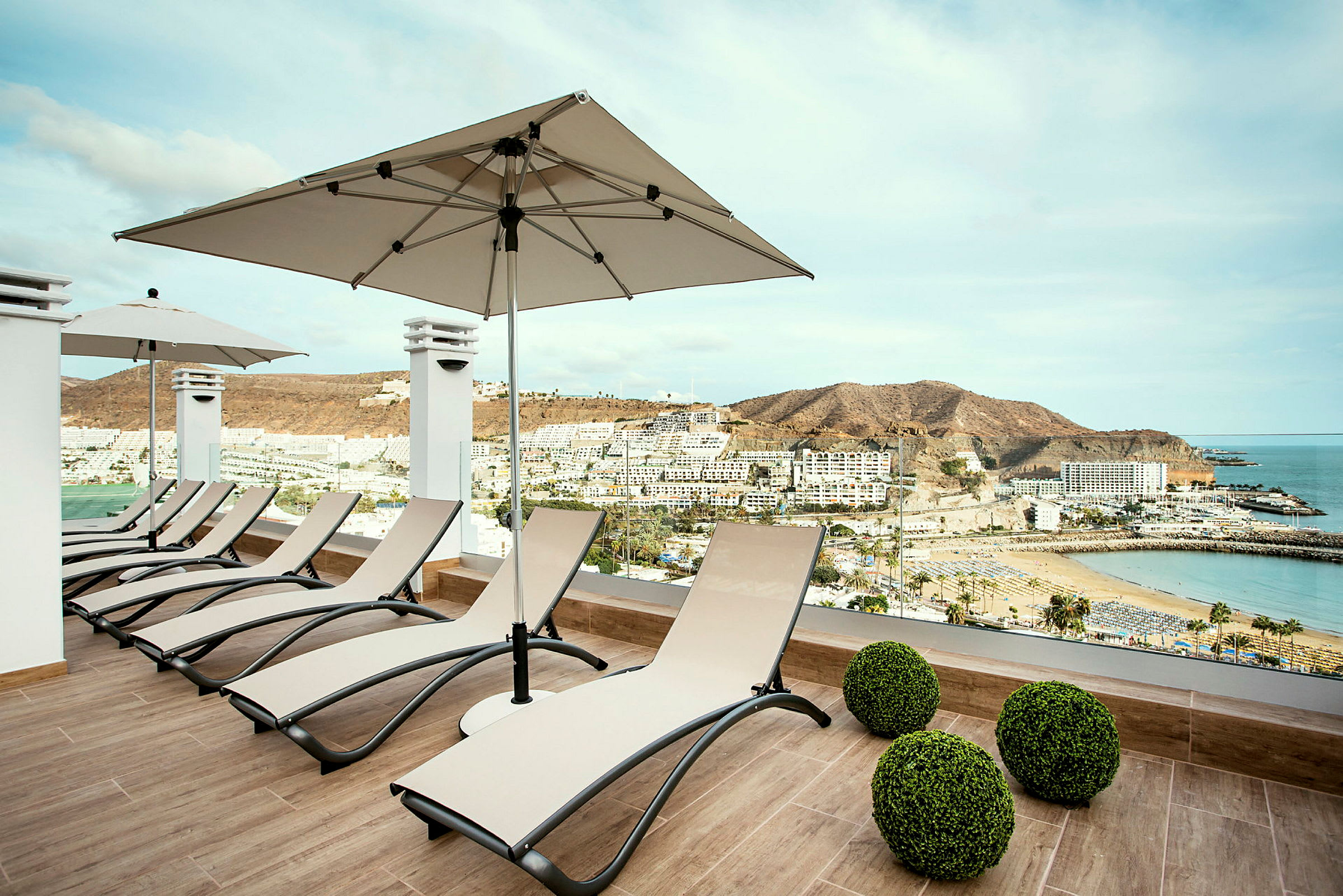 Solstolar på en terrass med utsikt över en strand och omgivande byggnader. (AI-genererad text)
