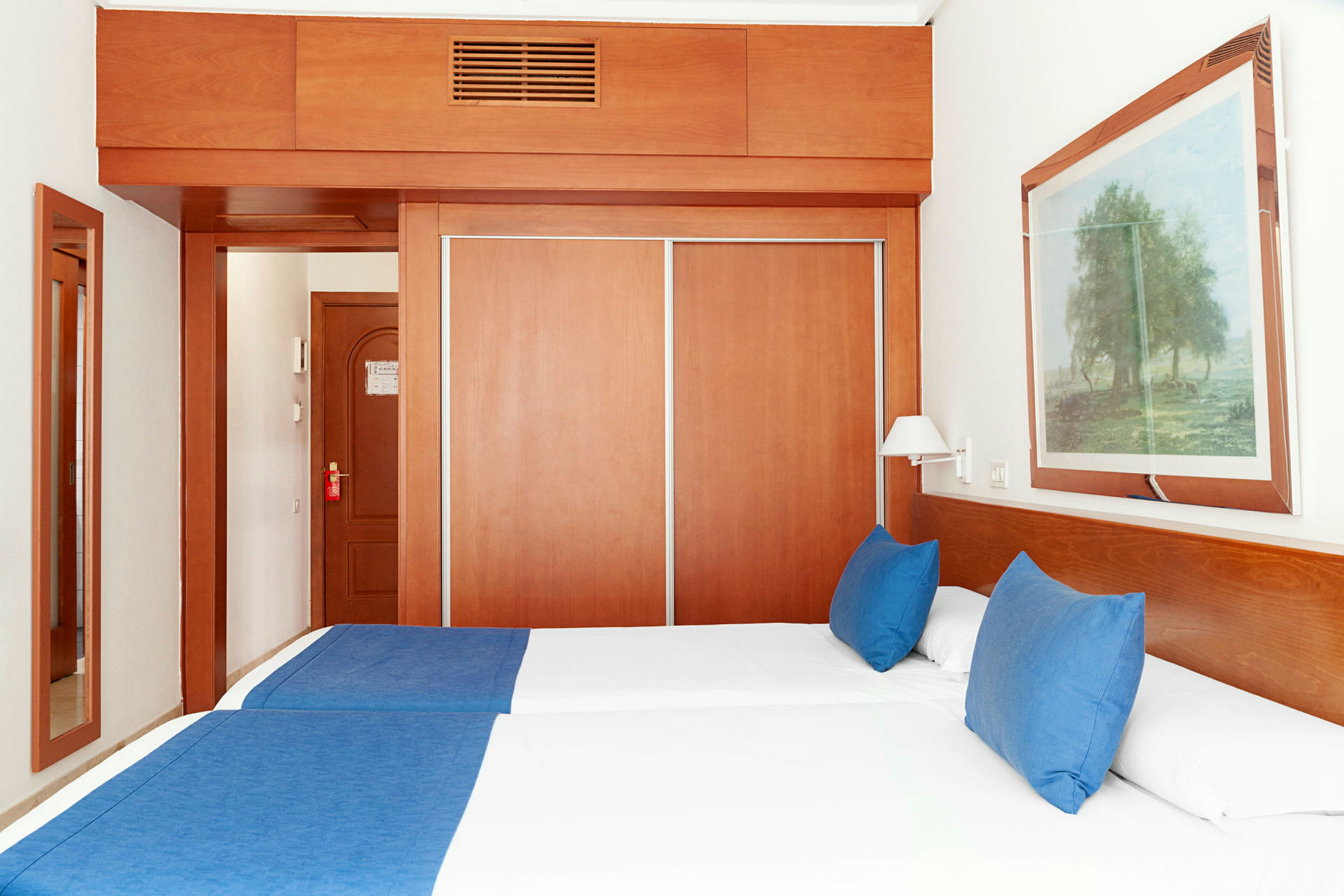 Hotellrum med två enkelsängar, blå sängkläder och en garderob med skjutdörrar. (AI-genererad text)