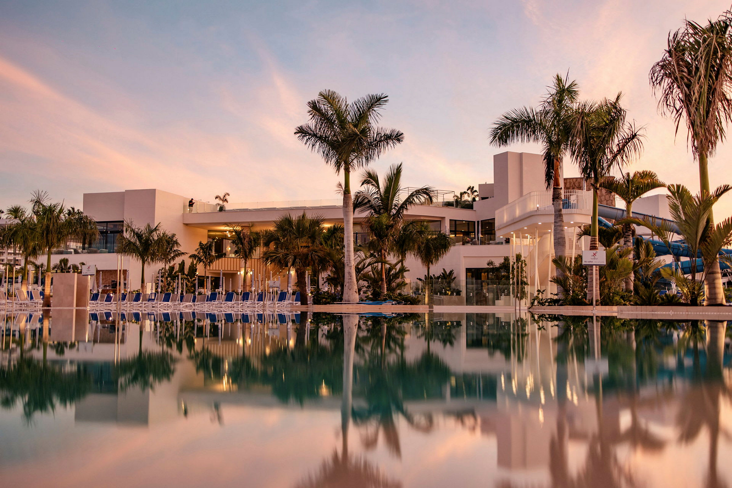 Hotellbyggnad och swimmingpool med spegelbild vid solnedgång. (AI-genererad text)