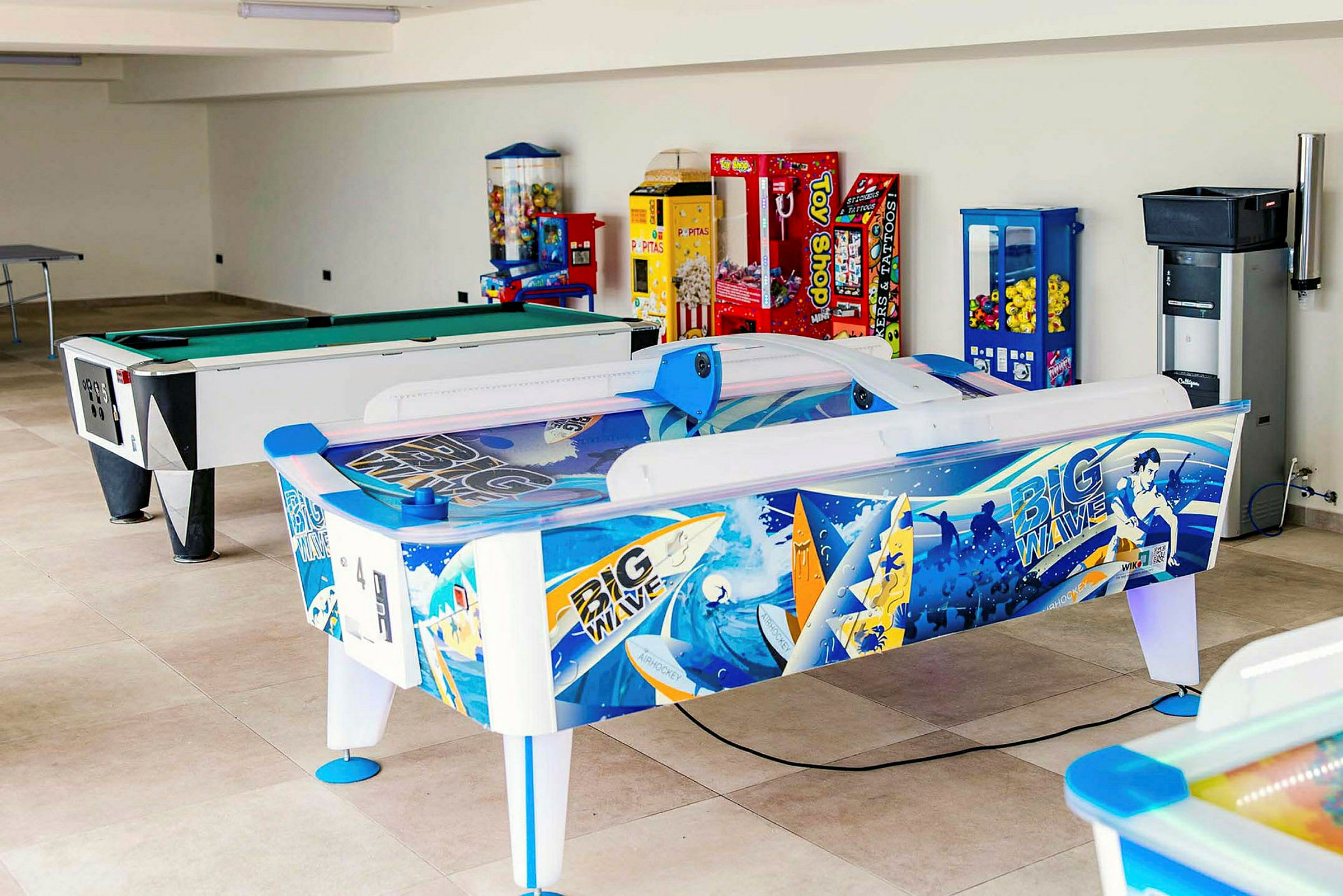 Ett spelrum med biljardbord, air hockey och olika spelautomater. (AI-genererad text)