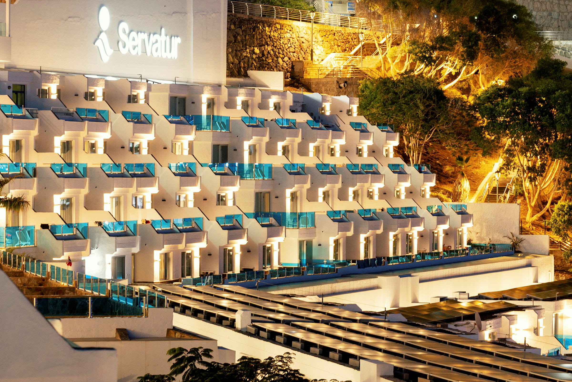 Flera upplysta hotellbyggnader med balkonger och omgivande träd. (AI-genererad text)